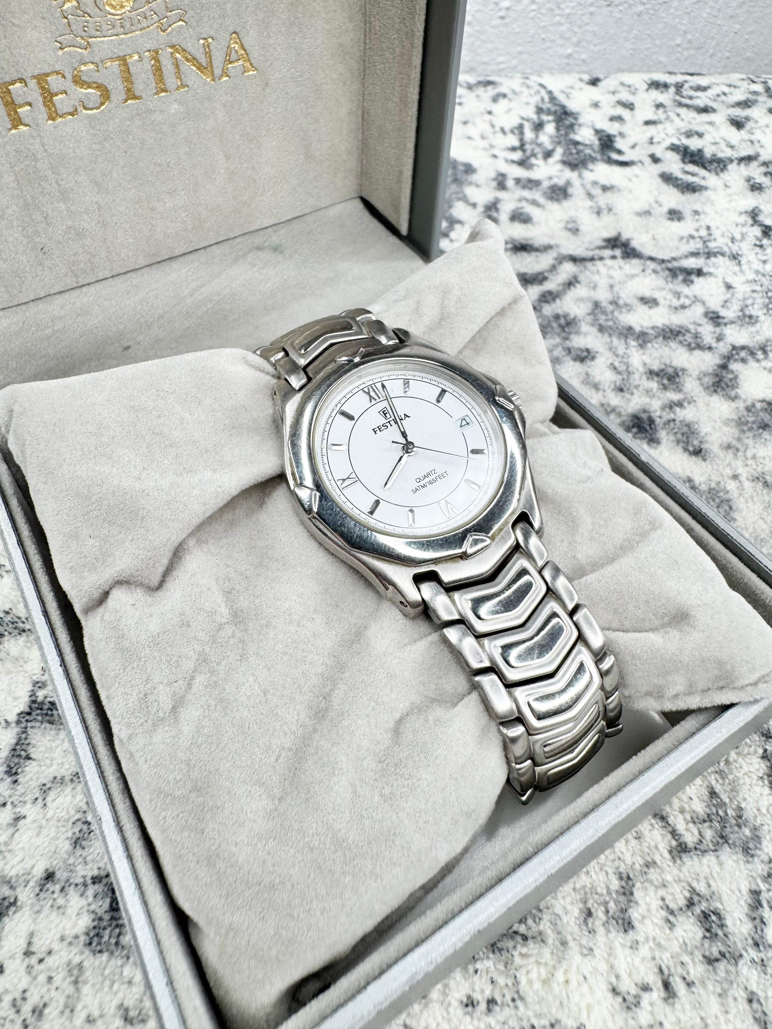 A Festina stainless steel watch with a silver link bracelet and white dial, presented inside its original gray box with a light gray velvet cushion. The brand name 'FESTINA' is visible in gold lettering on the inside lid.
