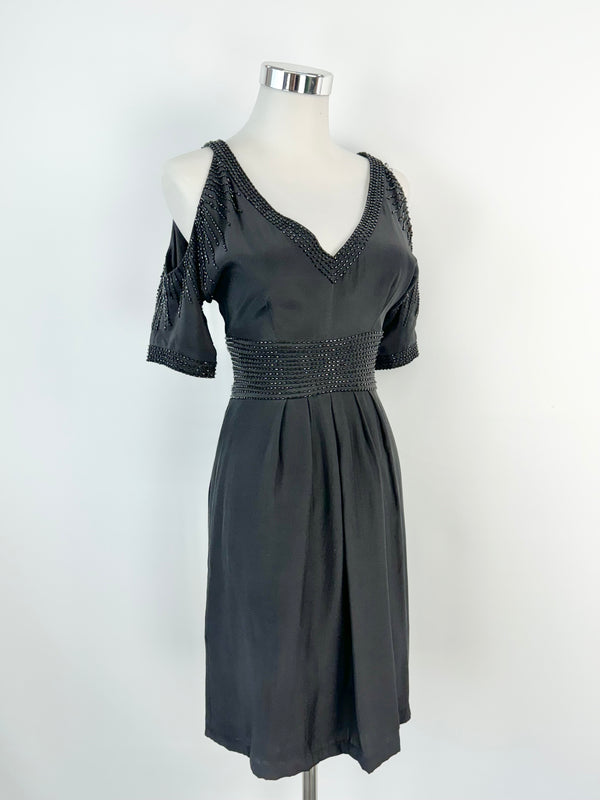 A black beaded midi dress with cut out shoulders and a v-neckline, displayed on a mannequin against a white background.