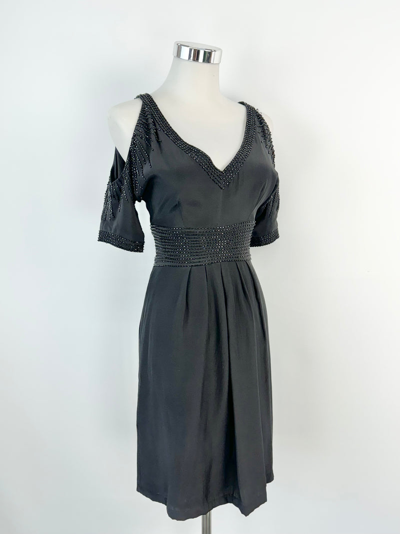 A black beaded midi dress with cut out shoulders and a v-neckline, displayed on a mannequin against a white background.