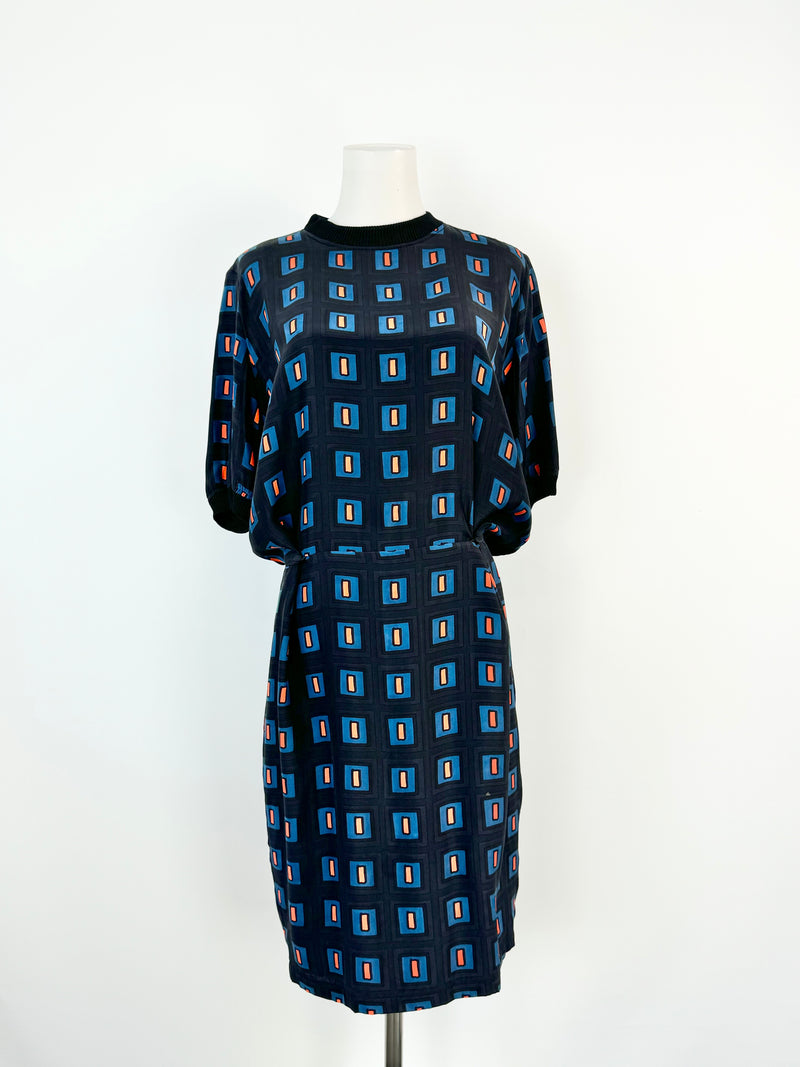 A silk sheath dress with a retro geometric pattern in blue and orange, featuring small buttons on the waist, a high neckline, and a wide rib knit trim.