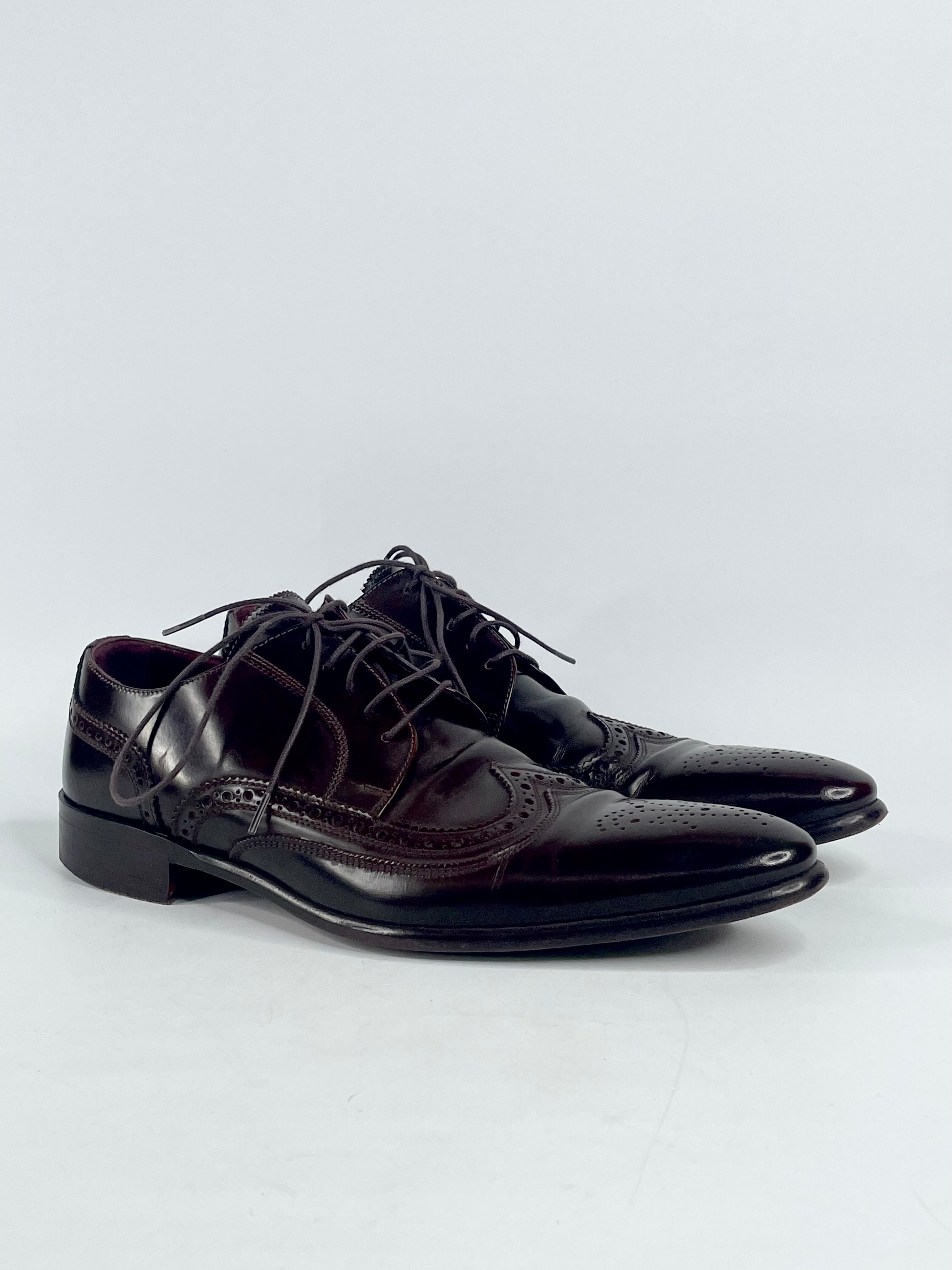 A pair of dark brown leather wing-tip Oxford shoes with visible signs of wear on the soles, placed on a plain background.