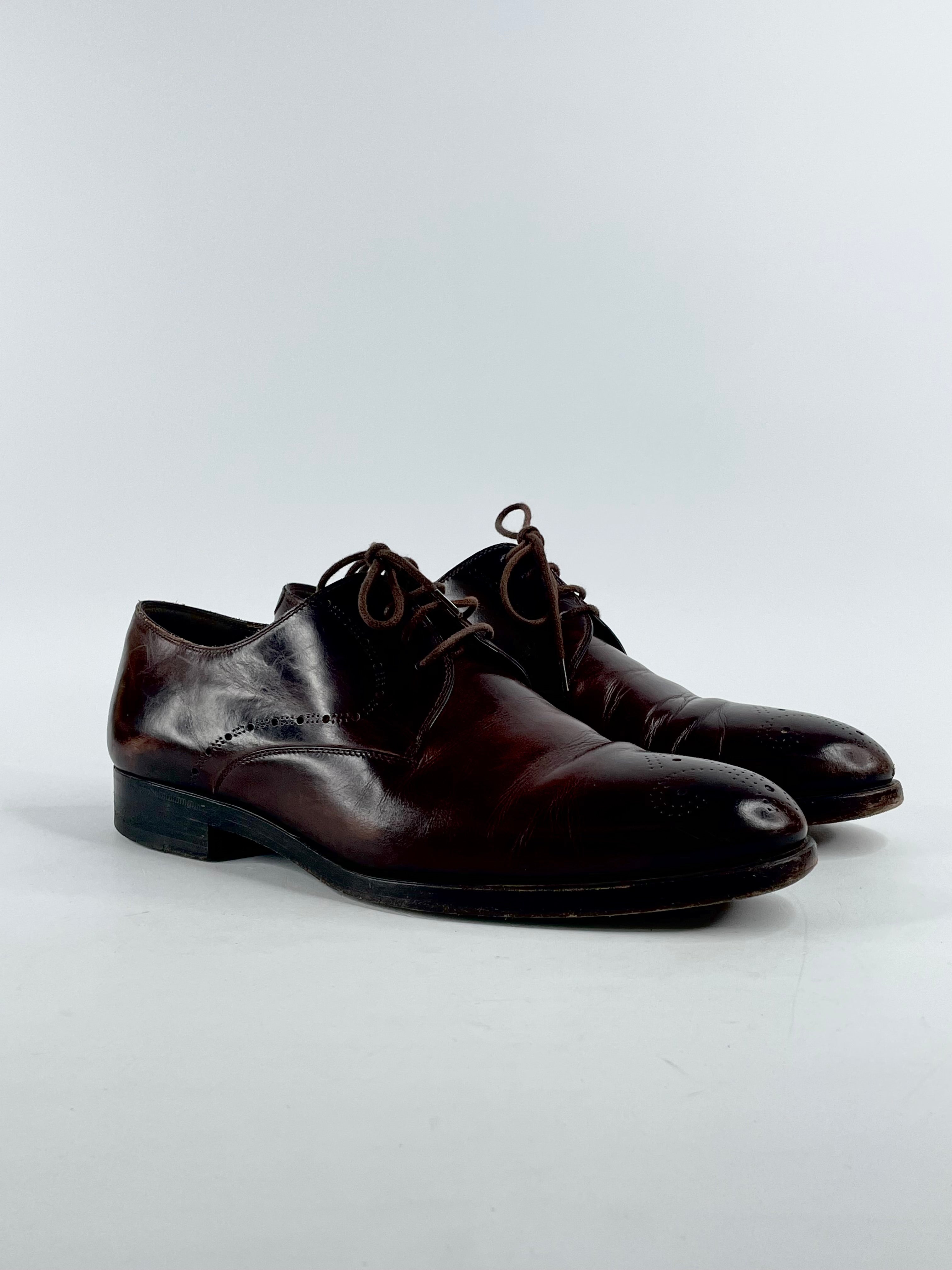 A pair of chestnut brown leather wing-top dress shoes with visible lace-up closure, on a white background.