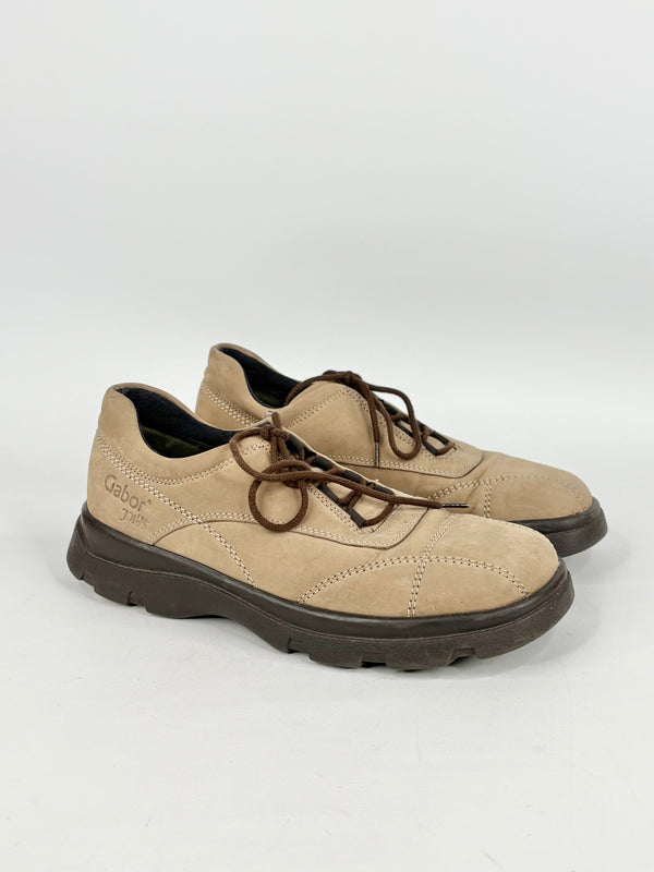 Pair of beige shoes with black soles on a white background