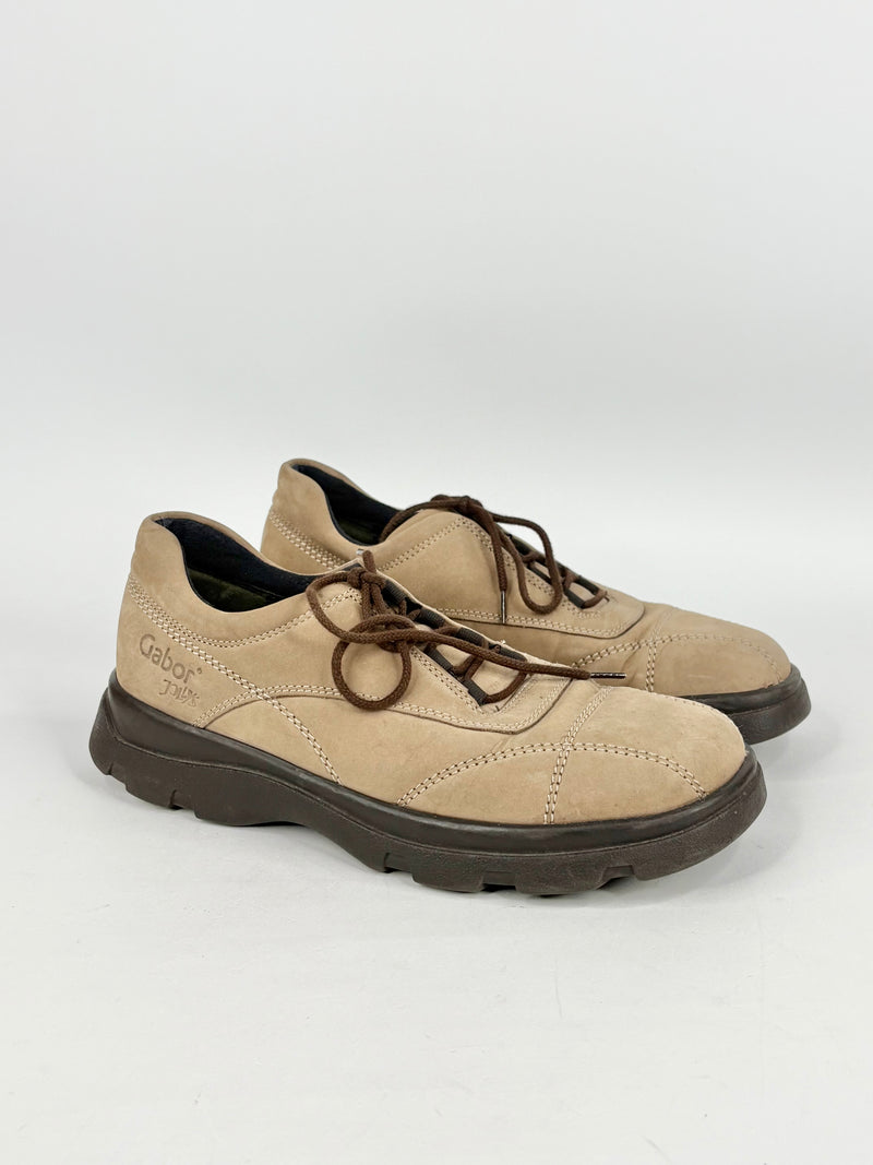 Pair of beige shoes with black soles on a white background