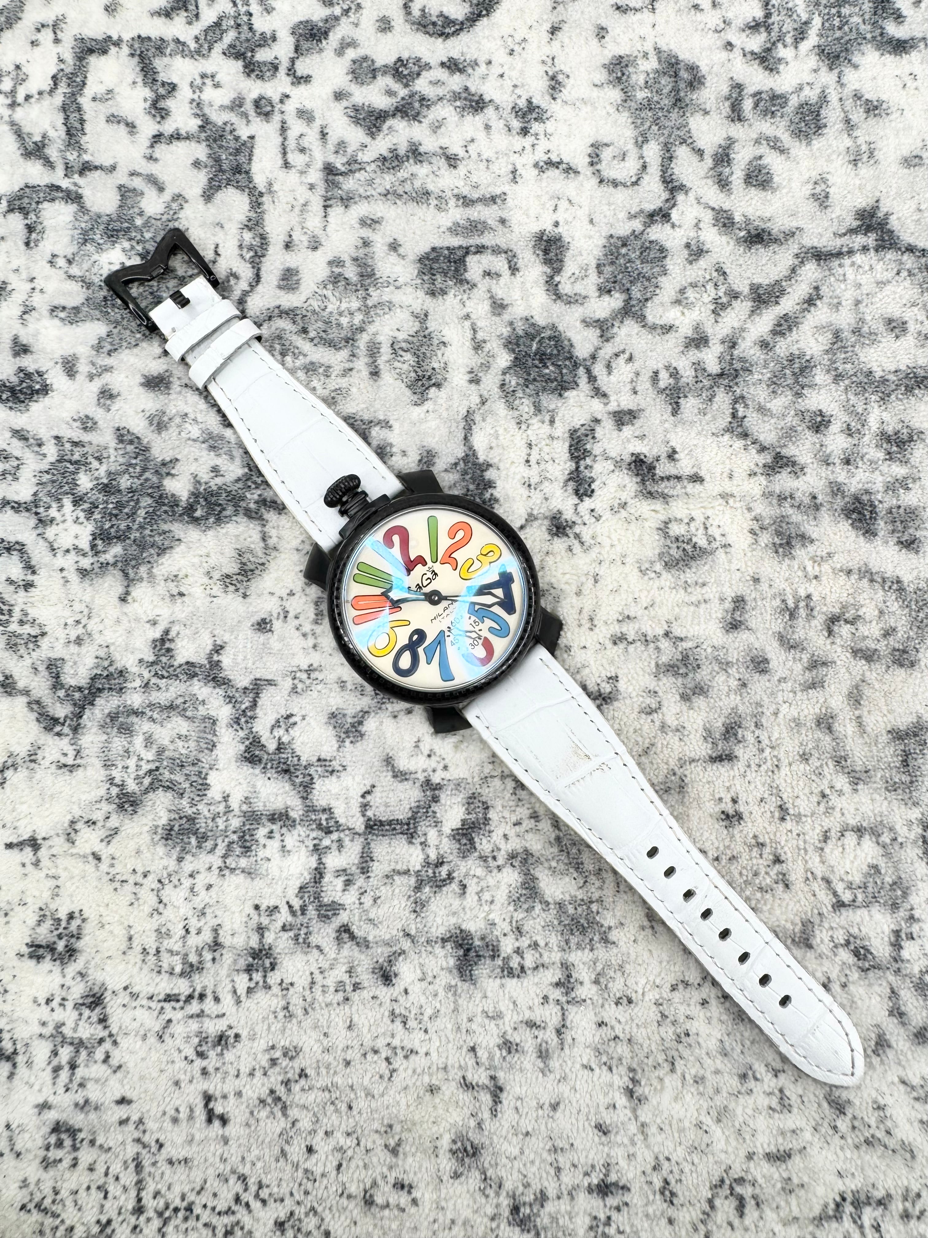 A wristwatch with a white leather strap, black case, and a colorful abstract dial, laid diagonally on a textured gray and white surface.