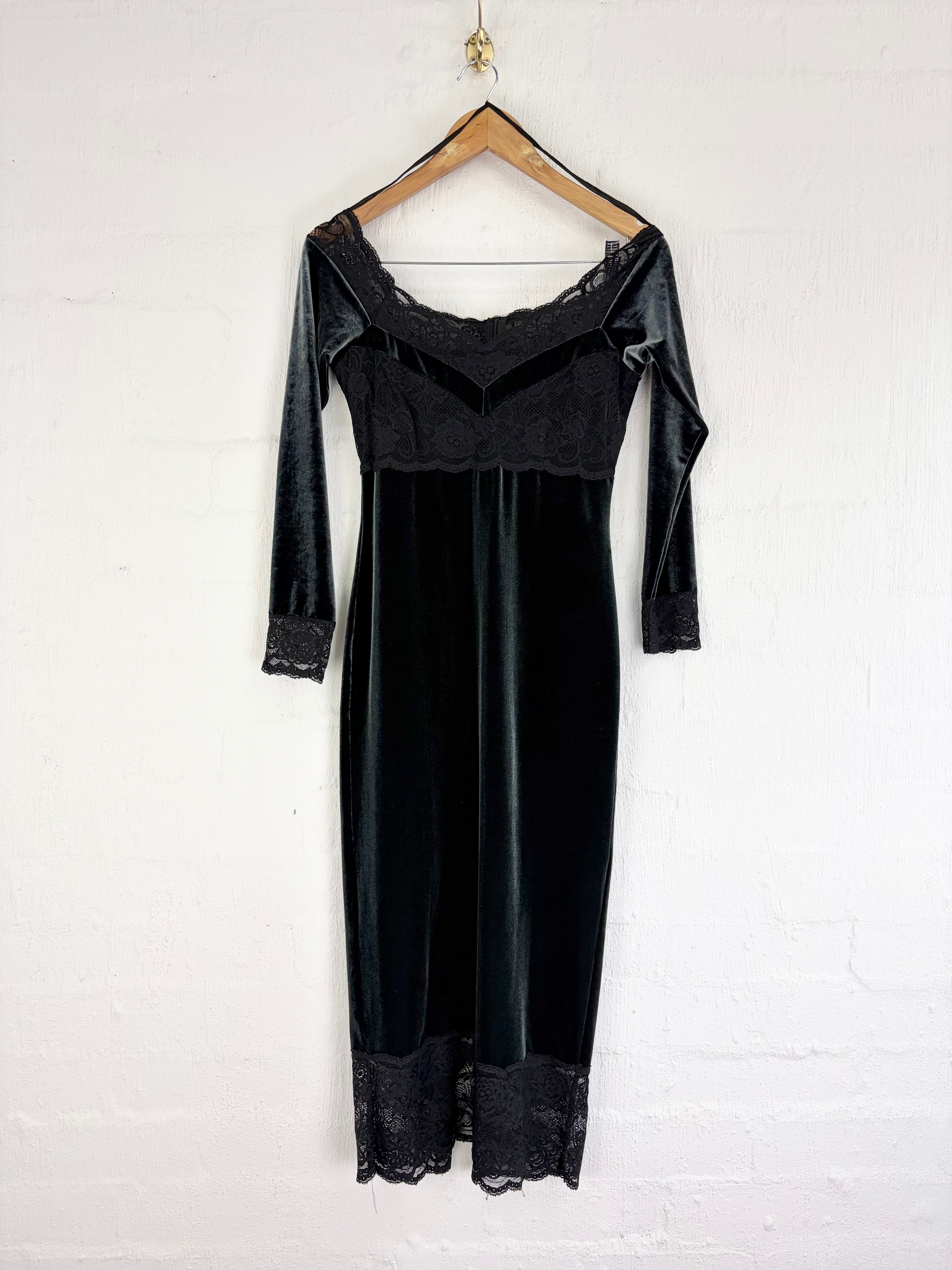 A black velvet nightgown with lace trim hanging on a wooden hanger against a white brick wall.