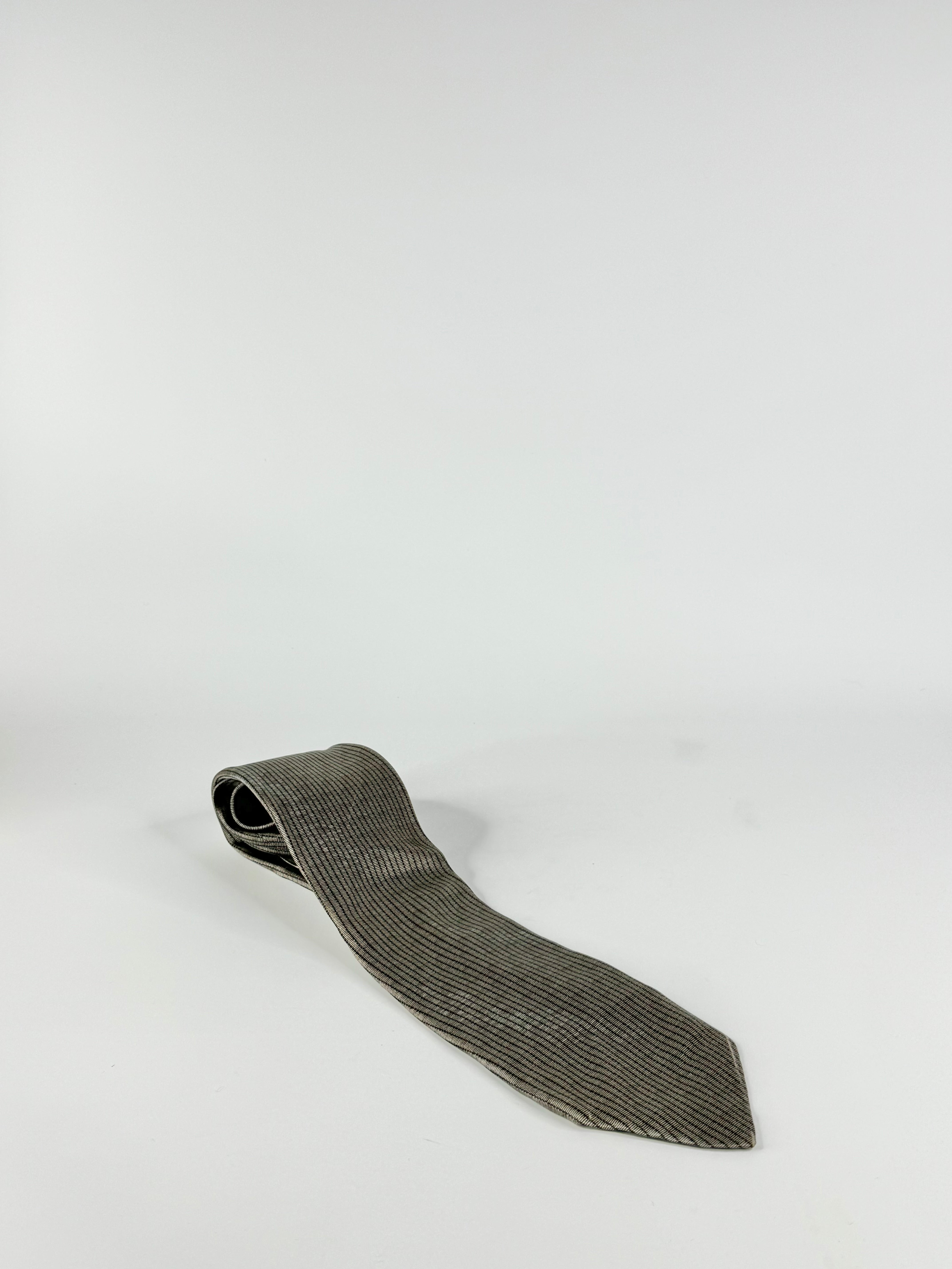 A silk patterned tie in taupe and black colors with a subtle geometric pattern, displayed against a white background.