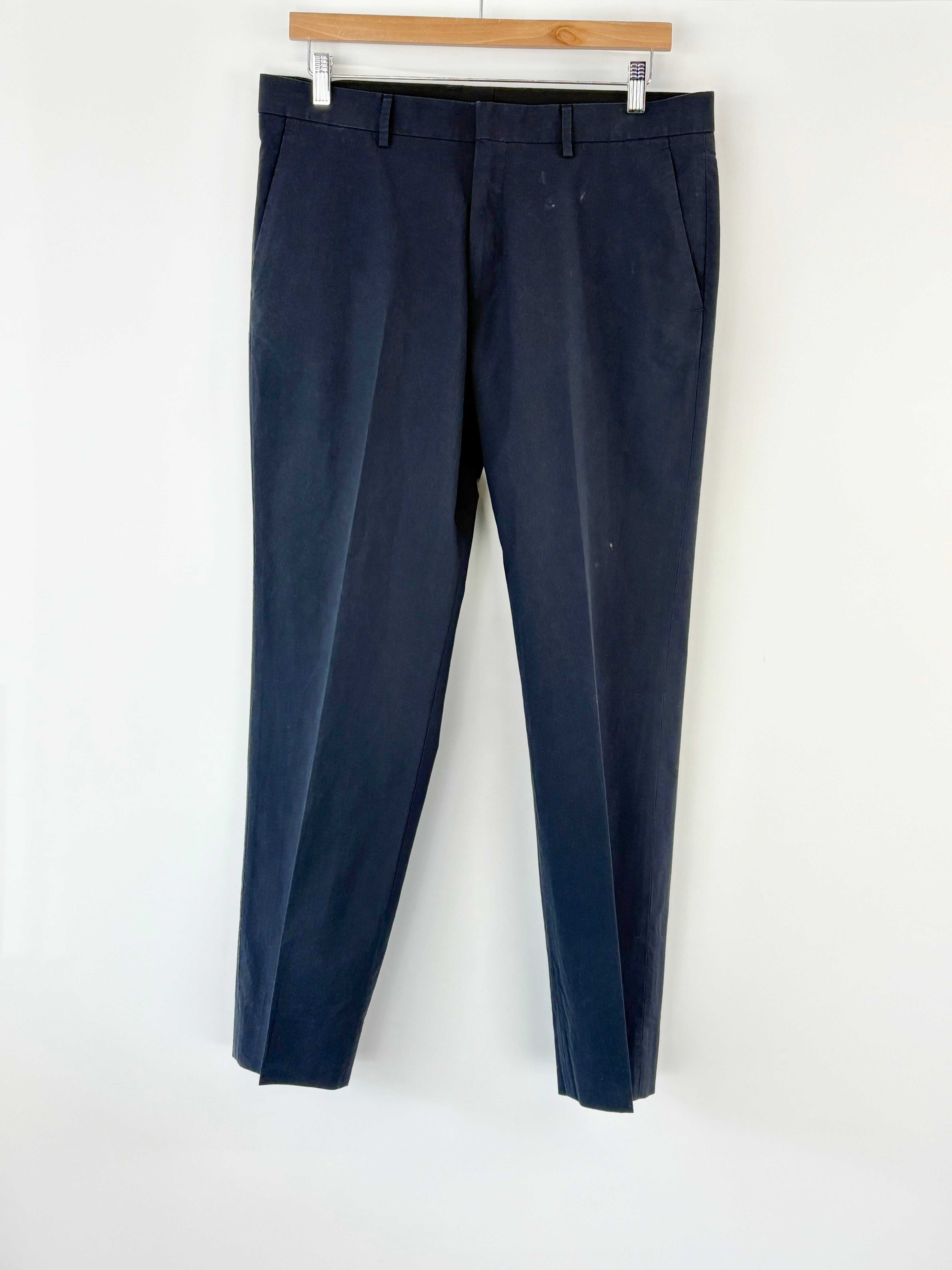 Navy blue pants hanging on a wooden hanger against a white wall