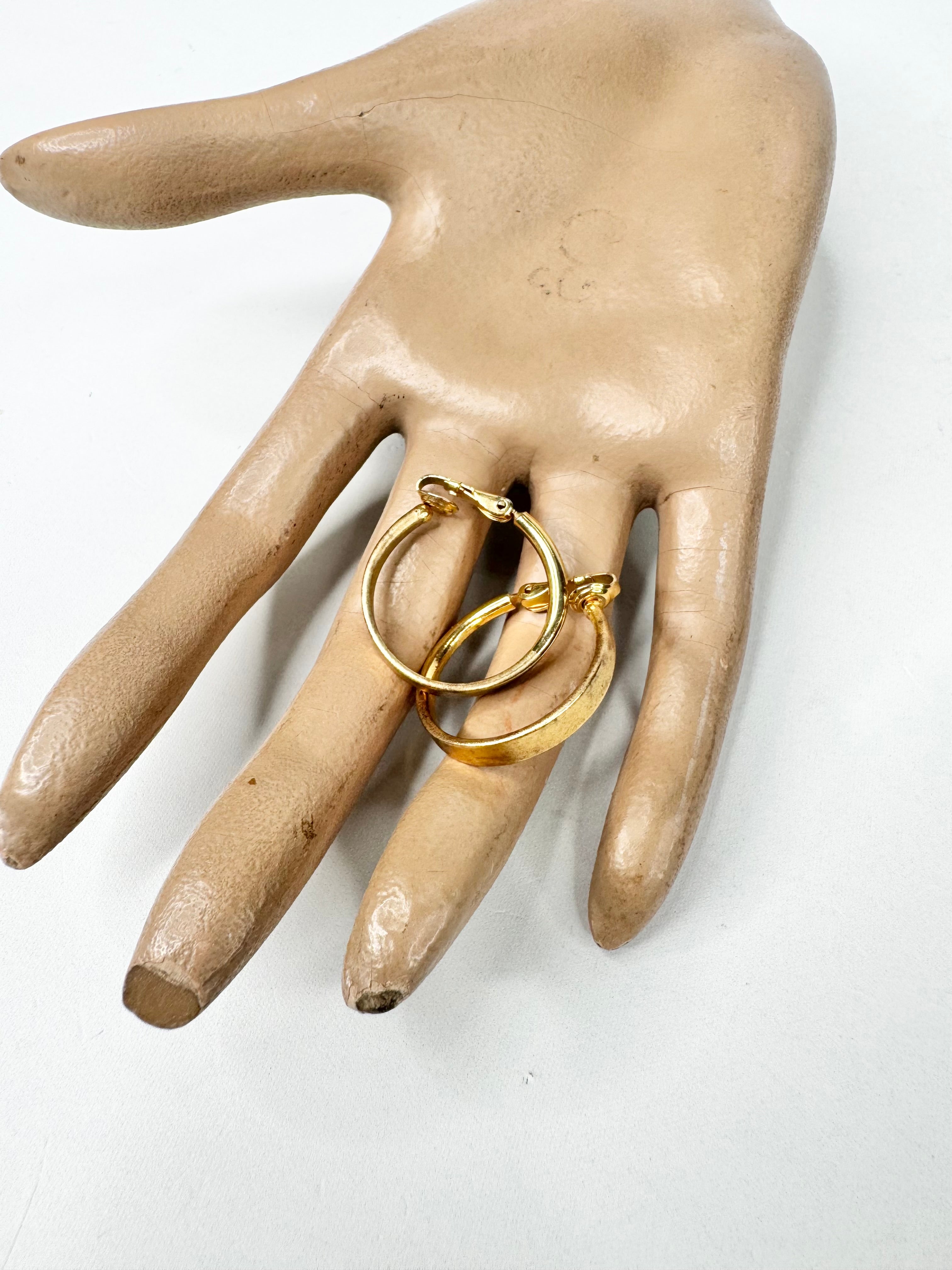Gold hoop earrings on a mannequin hand against a white background