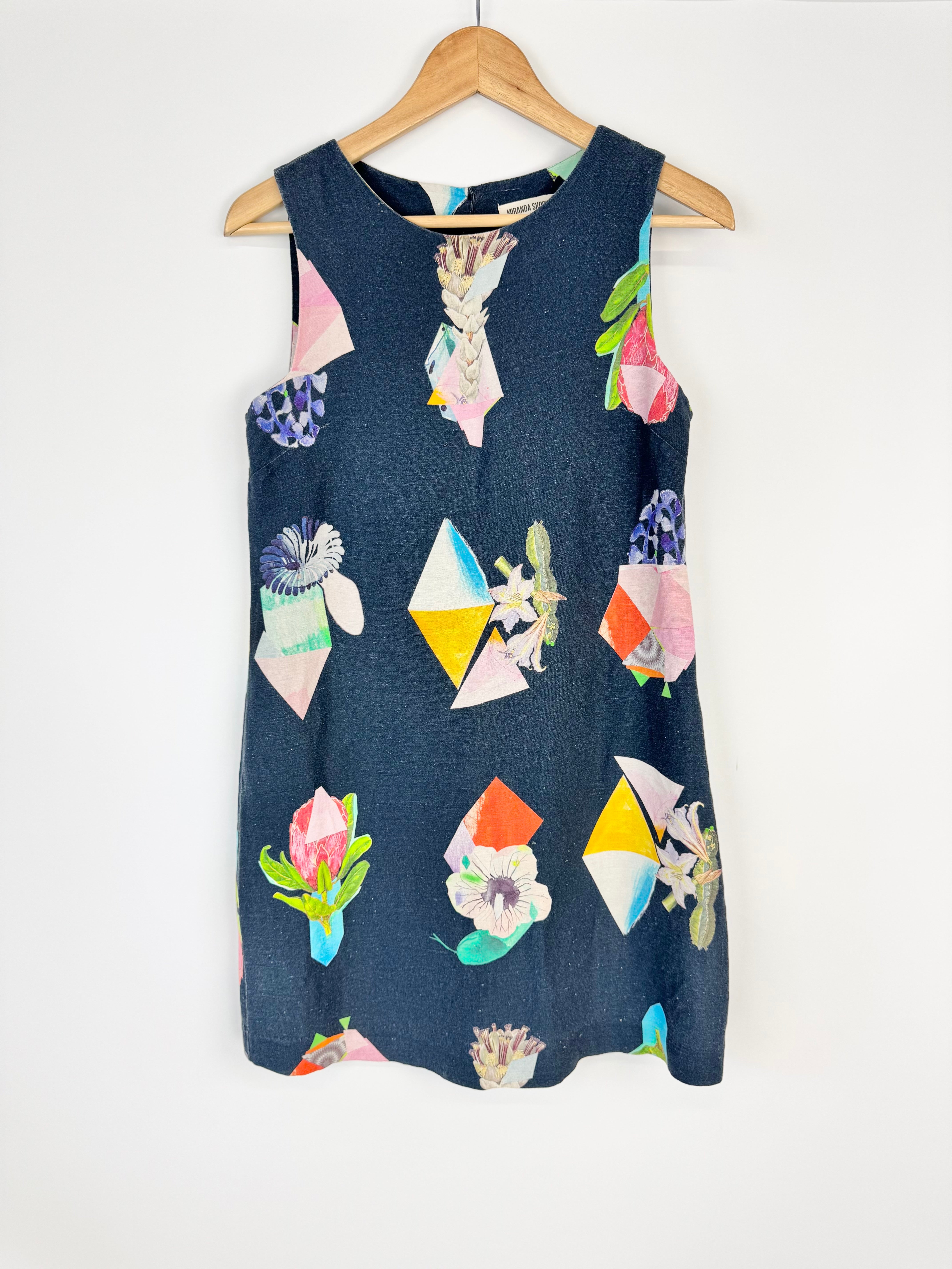 Blue sleeveless dress with colorful geometric pattern on a wooden hanger against a white background