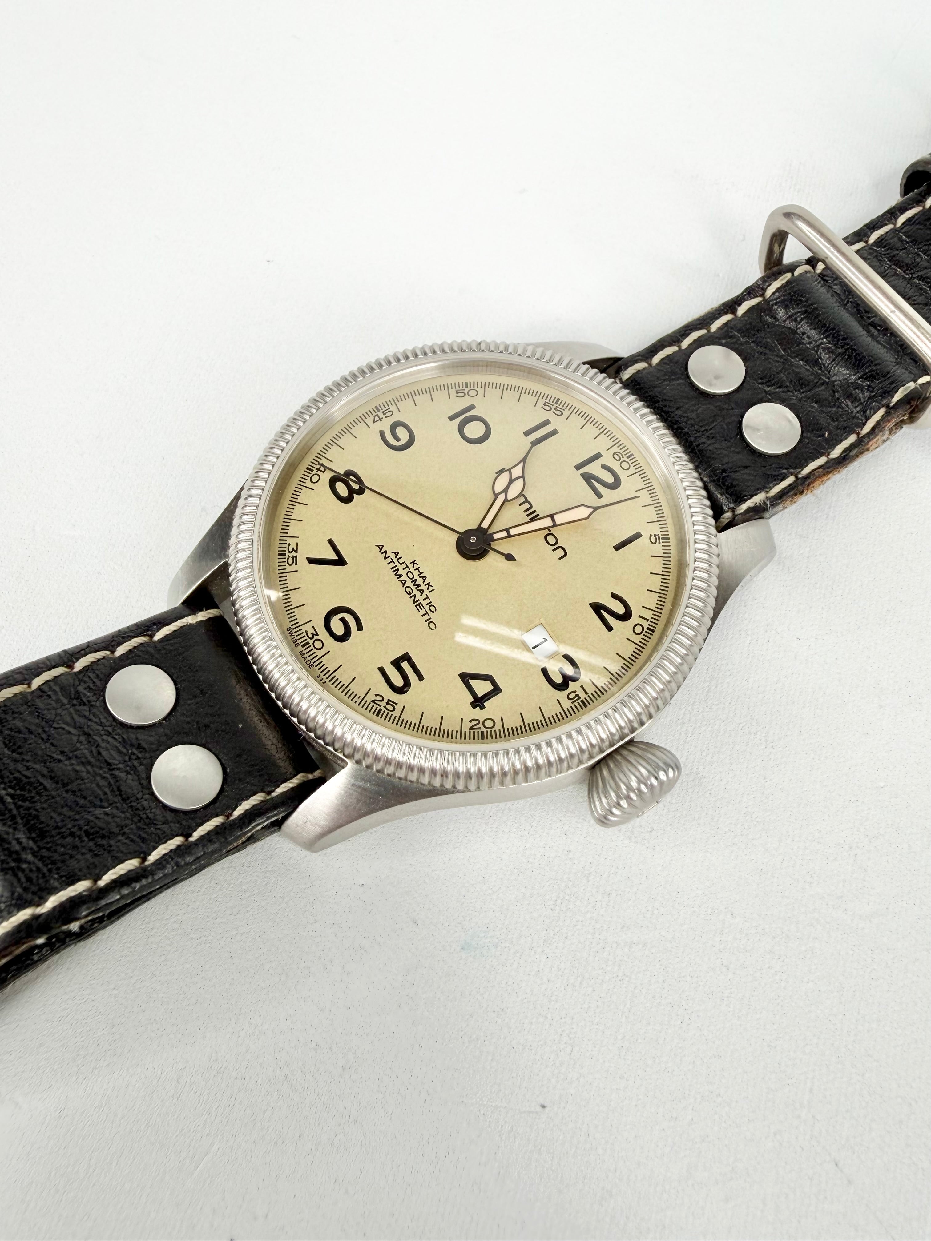 Vintage wristwatch with black leather strap and beige dial on a white background