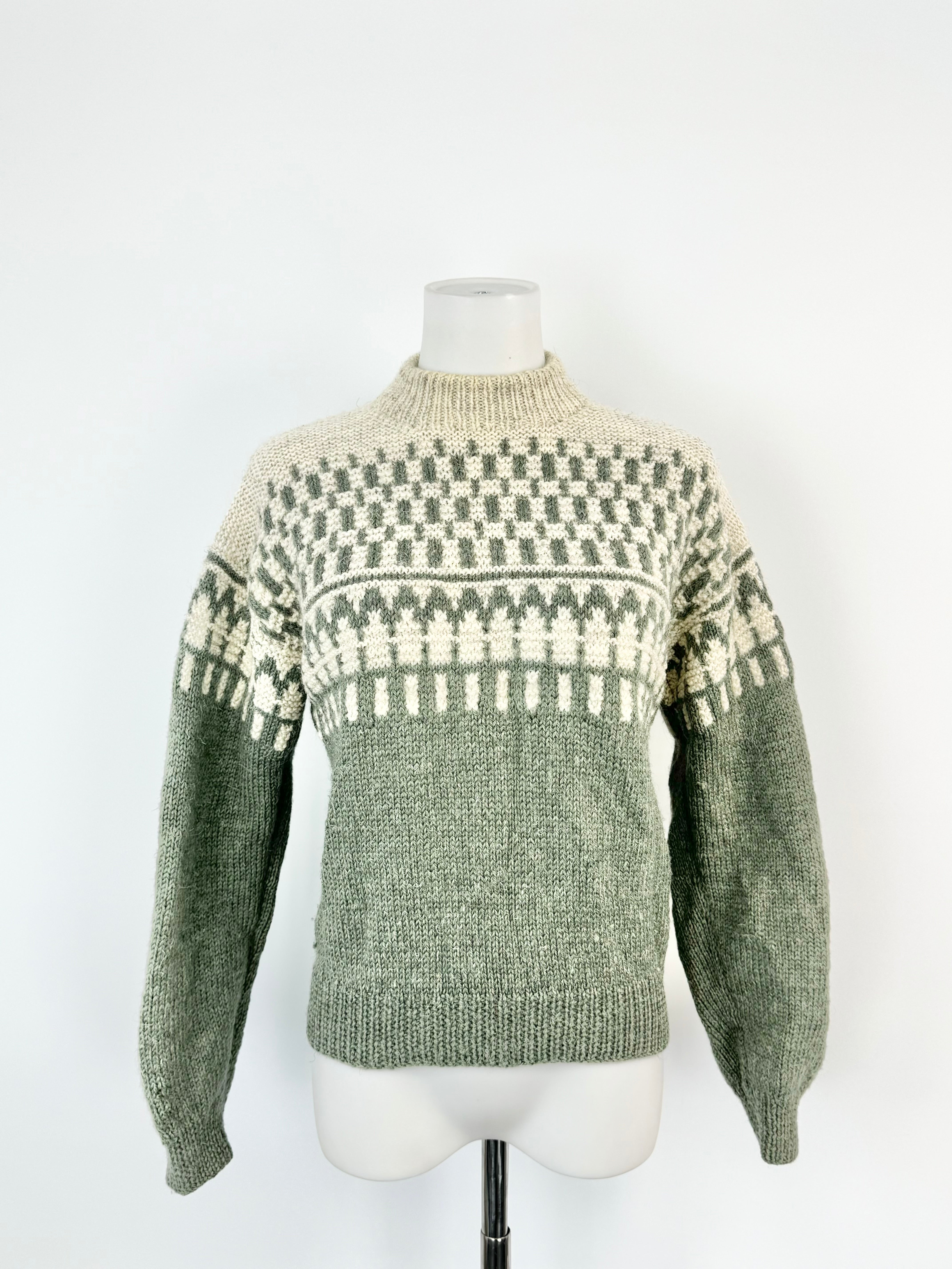 A hand-knitted sage green and white jumper displayed on a mannequin with a high neckline and puffed sleeves.