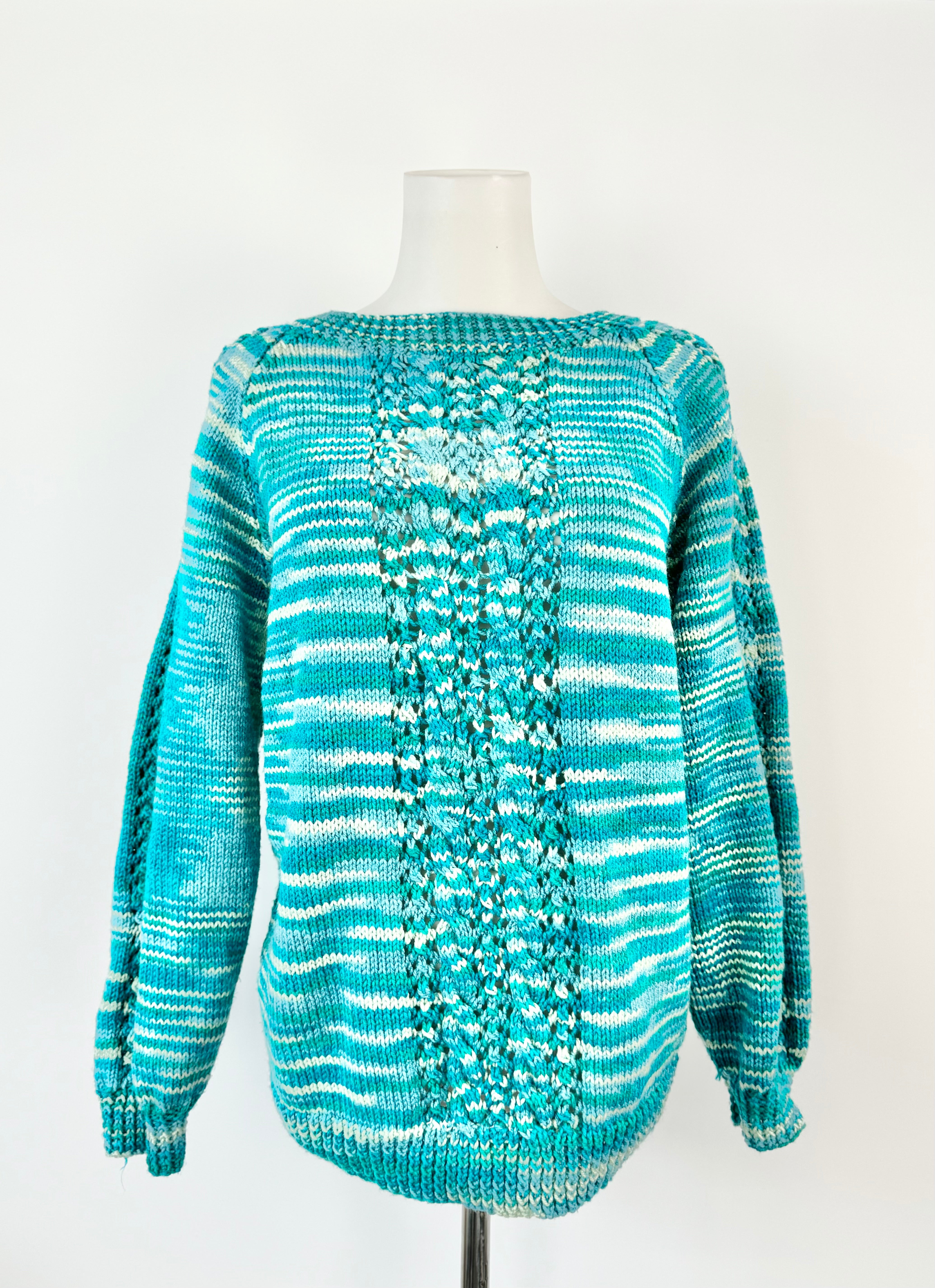 A hand knitted blue acrylic jumper with a high crew neckline and cable knit patterns on the sleeves and shoulders, displayed on a mannequin.
