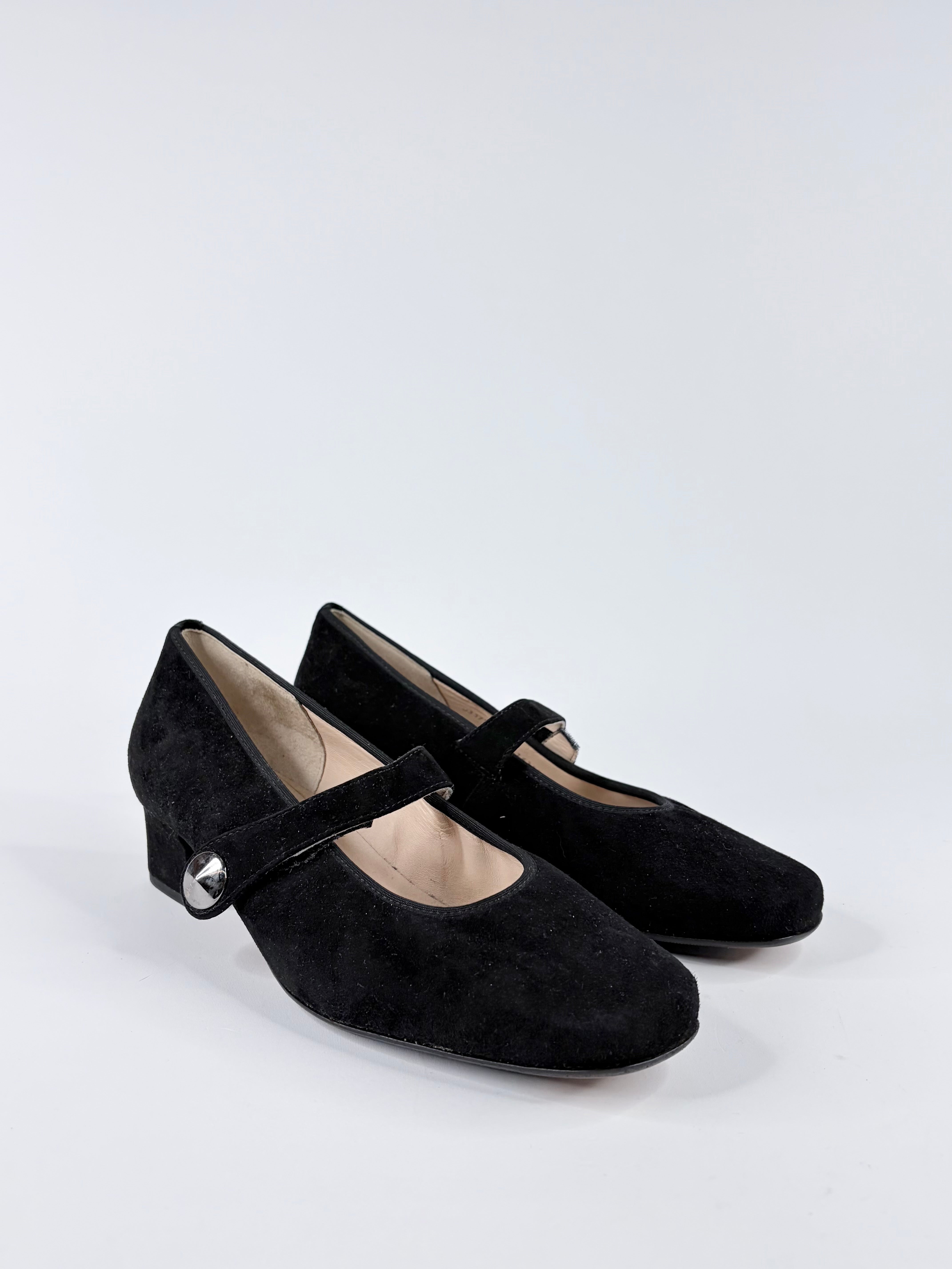 Pair of black suede shoes with a strap on a white background