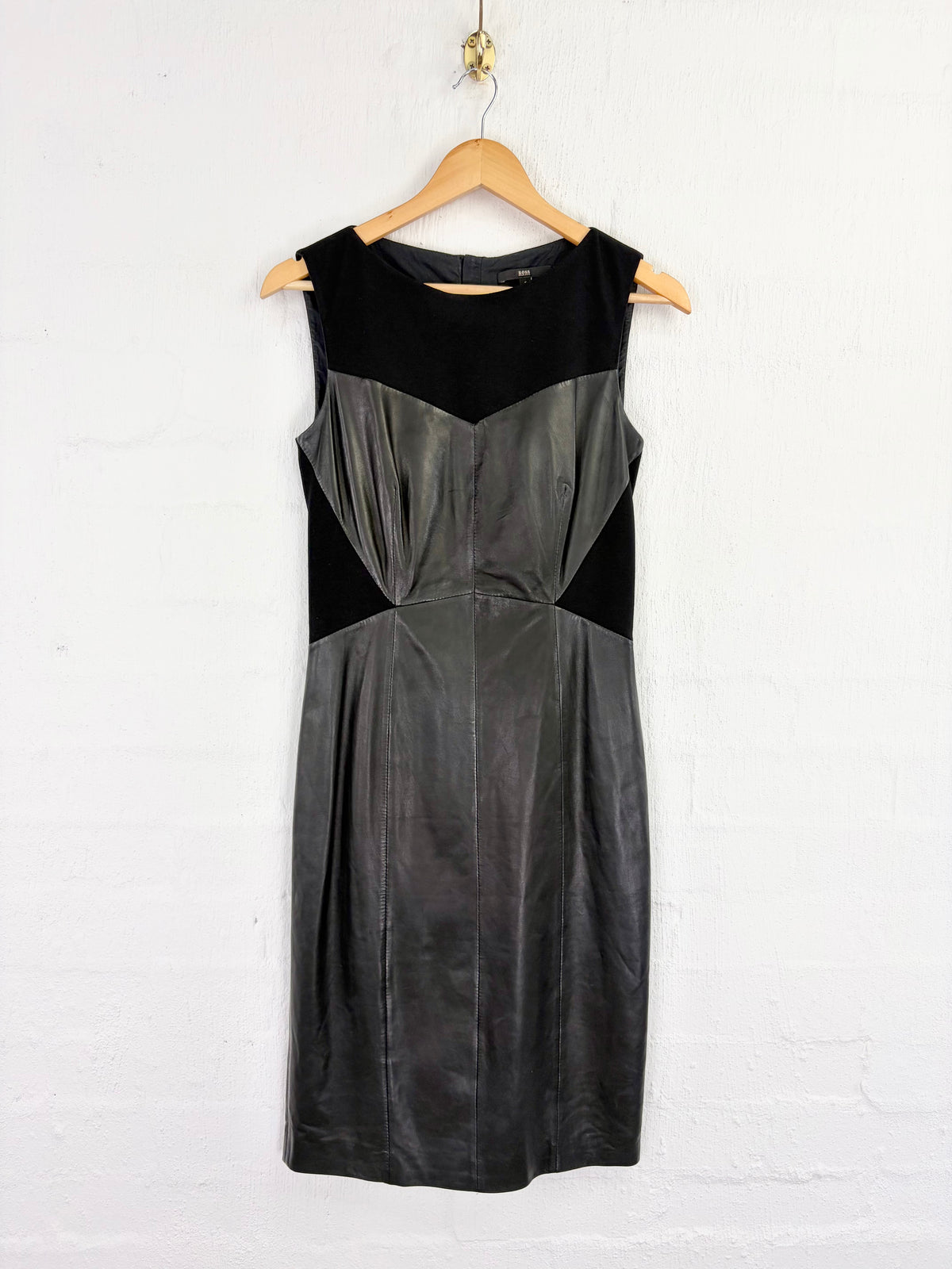 A sleeveless black and dark gray color-block dress hanging on a wooden hanger against a white painted brick wall.