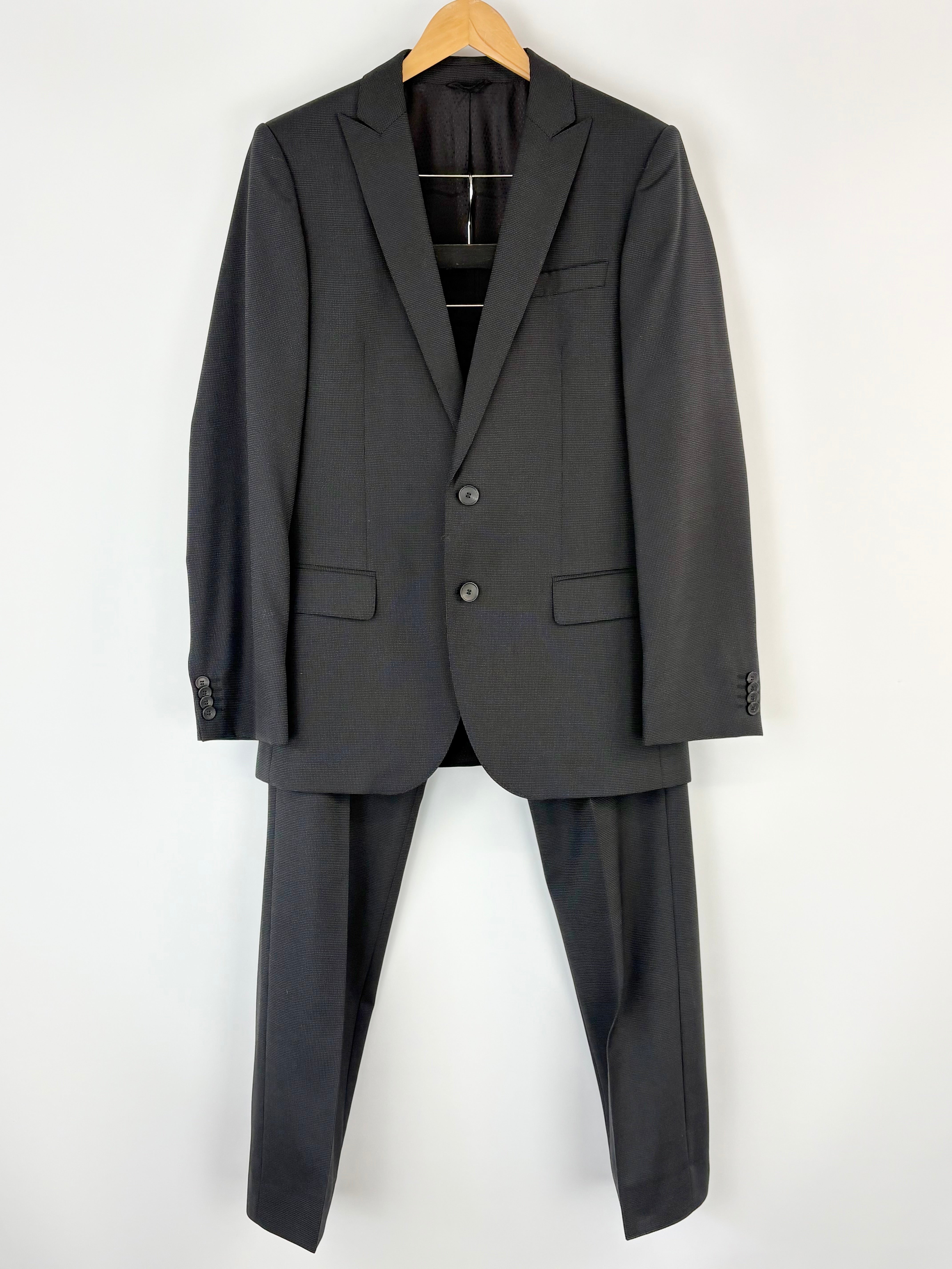 Black Hugo Boss suit jacket and pants on a hanger against a white background