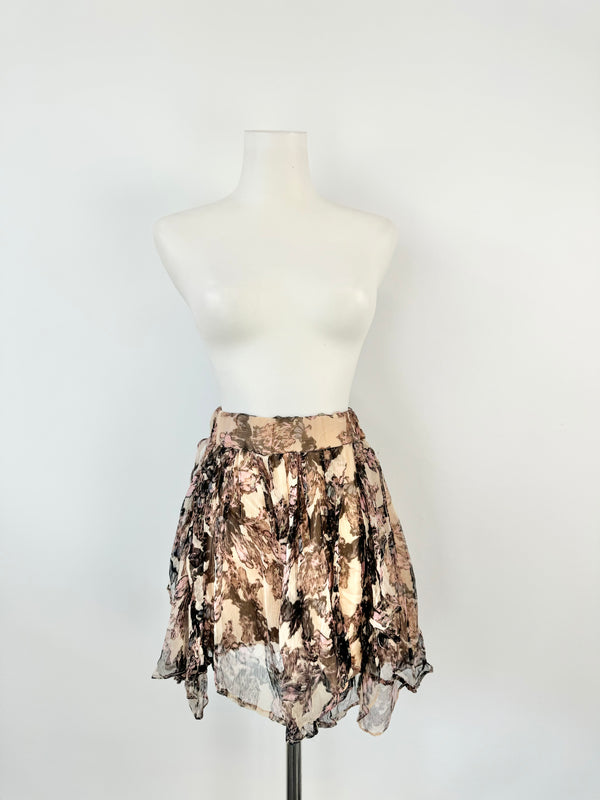A mannequin displaying a midi-length skirt with a floral pattern in purple and pink colors, featuring a medium-wide elastic band waist and an asymmetrical hem.