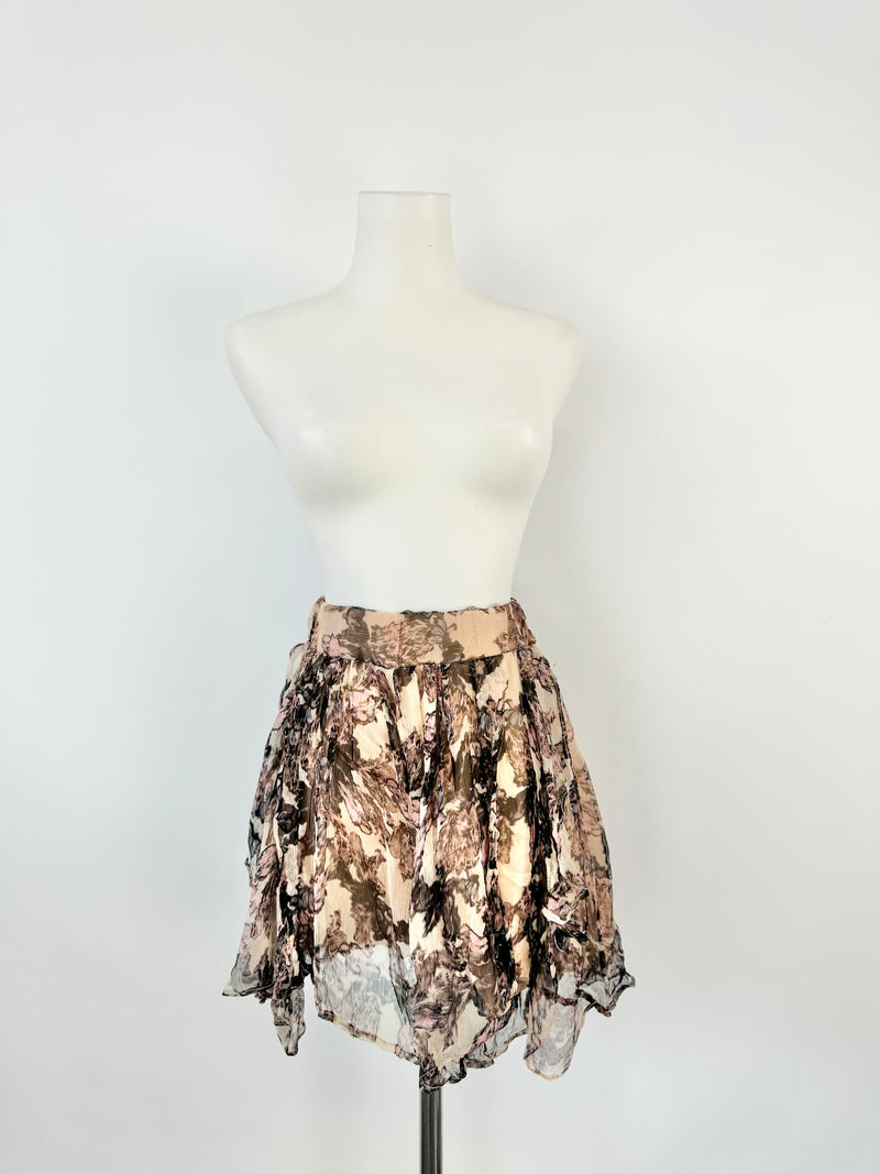 A mannequin displaying a midi-length skirt with a floral pattern in purple and pink colors, featuring a medium-wide elastic band waist and an asymmetrical hem.