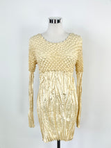 A pleated metallic gold dress with long sleeves displayed on a mannequin.