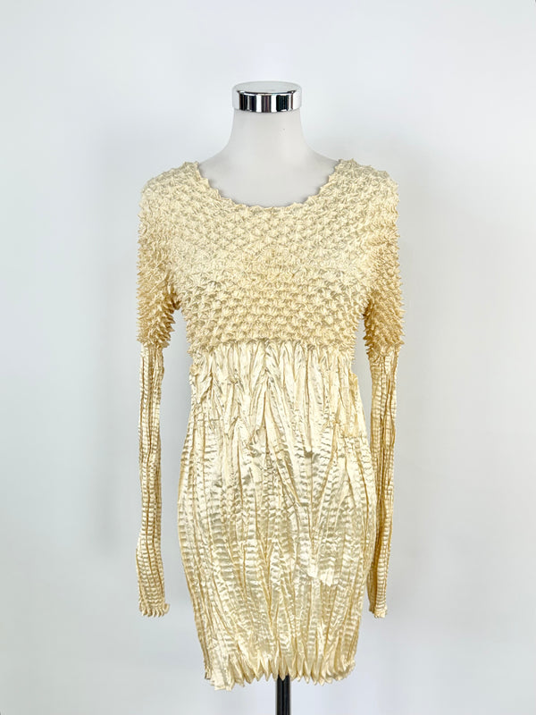A pleated metallic gold dress with long sleeves displayed on a mannequin.