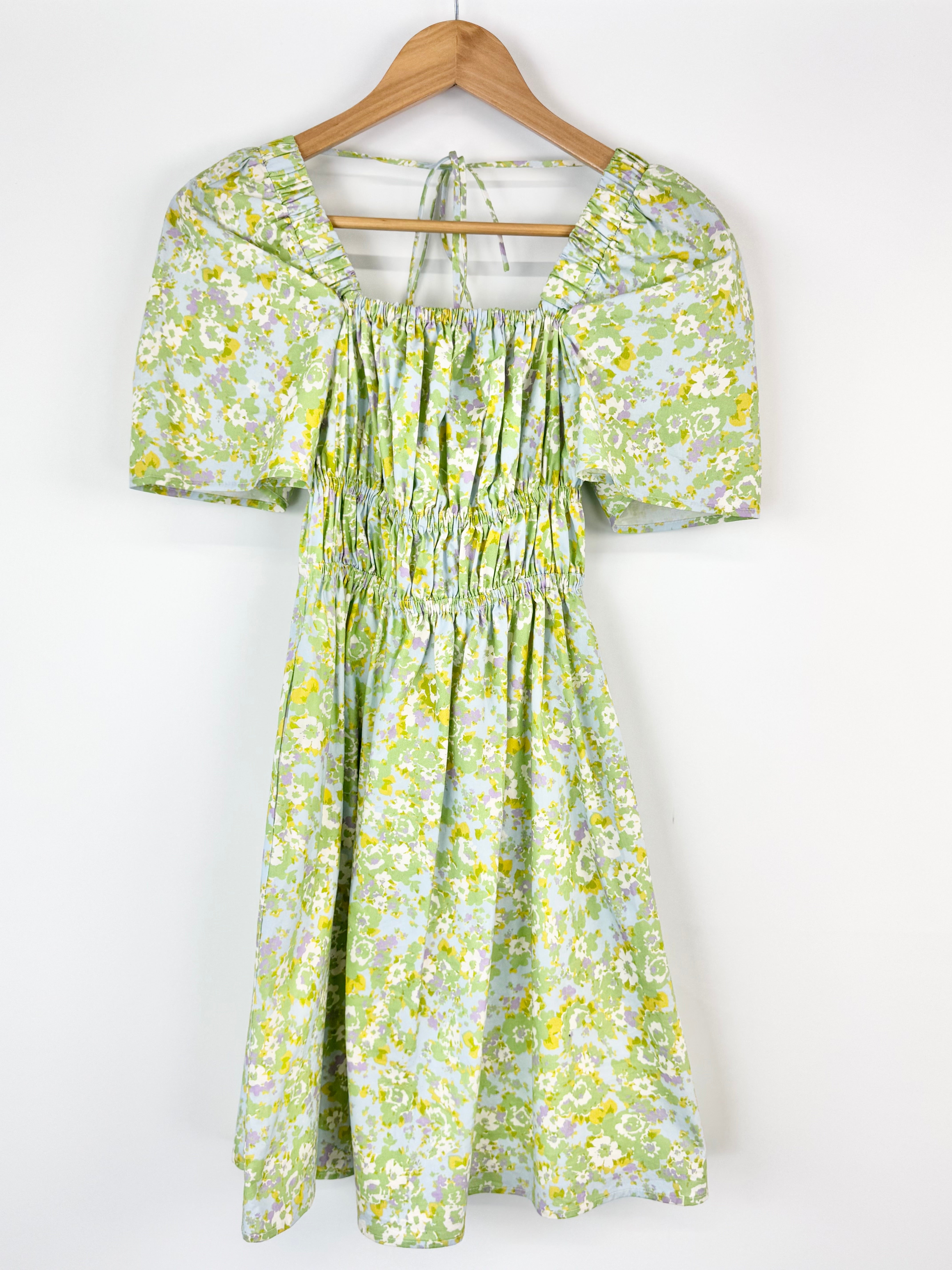 Green floral dress on a wooden hanger against a white background