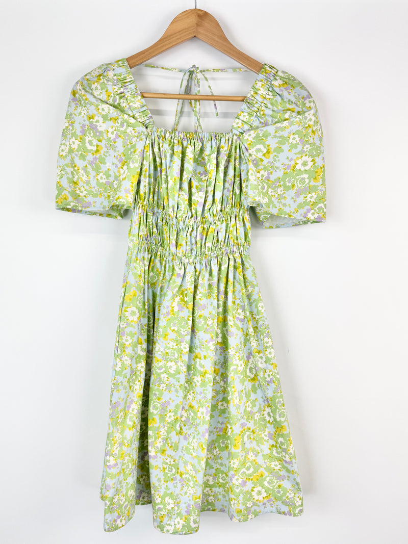 Green floral dress on a wooden hanger against a white background