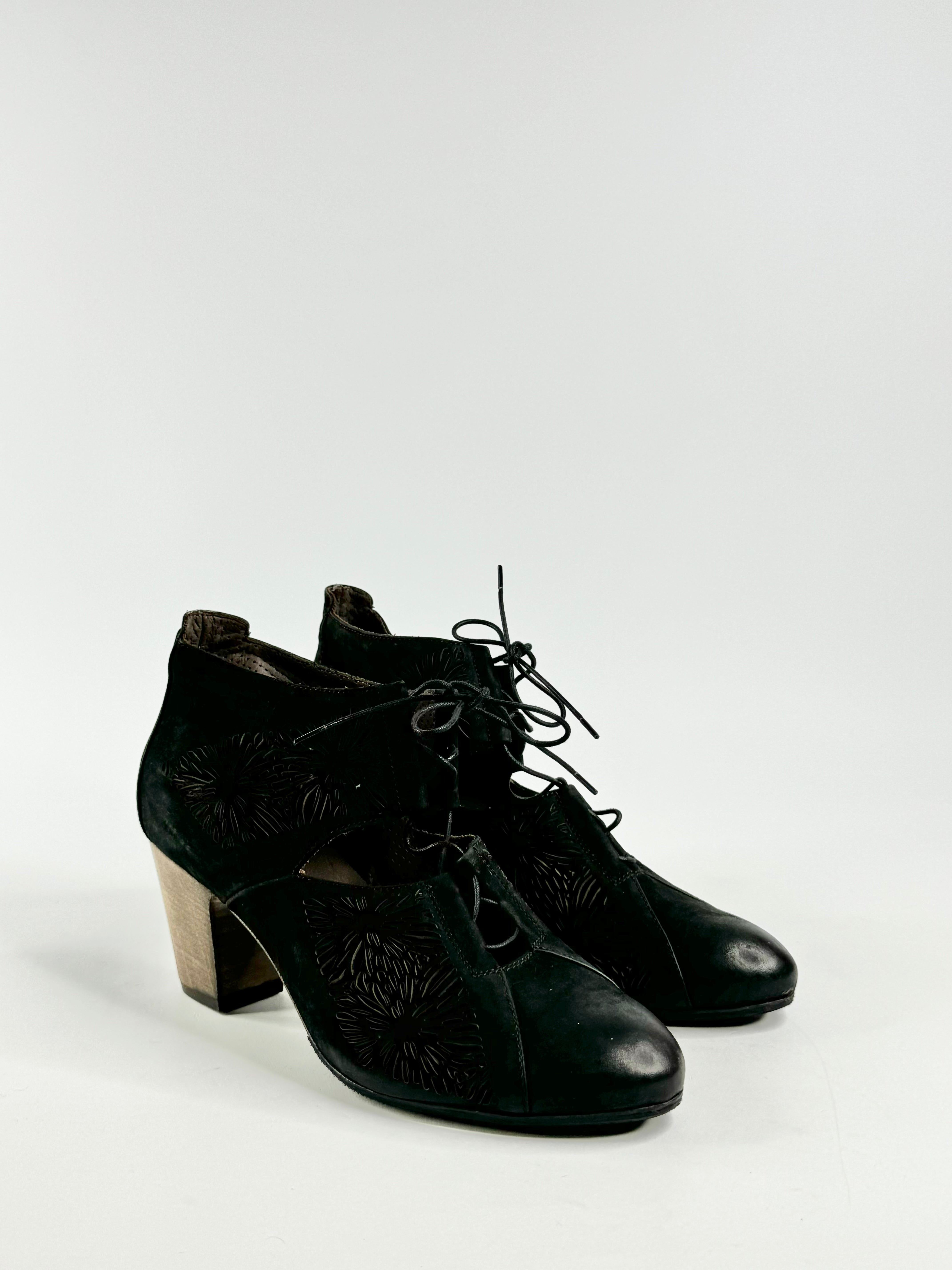 A pair of black, lace-up, block heeled shoes with side lazer cut detailing on a white background.
