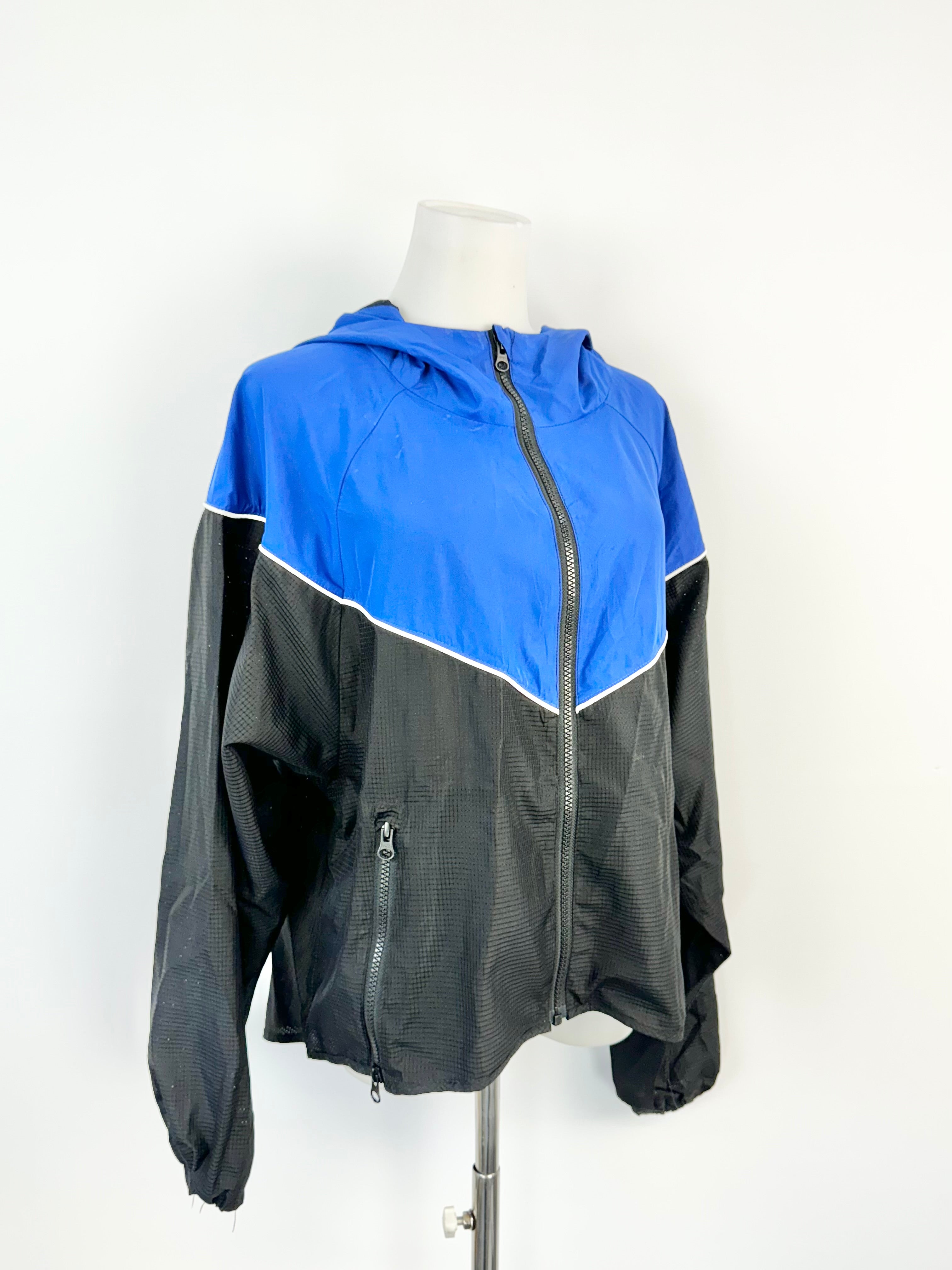 A blue and black contrast windbreaker jacket on a mannequin, with a relaxed fit and a hood.
