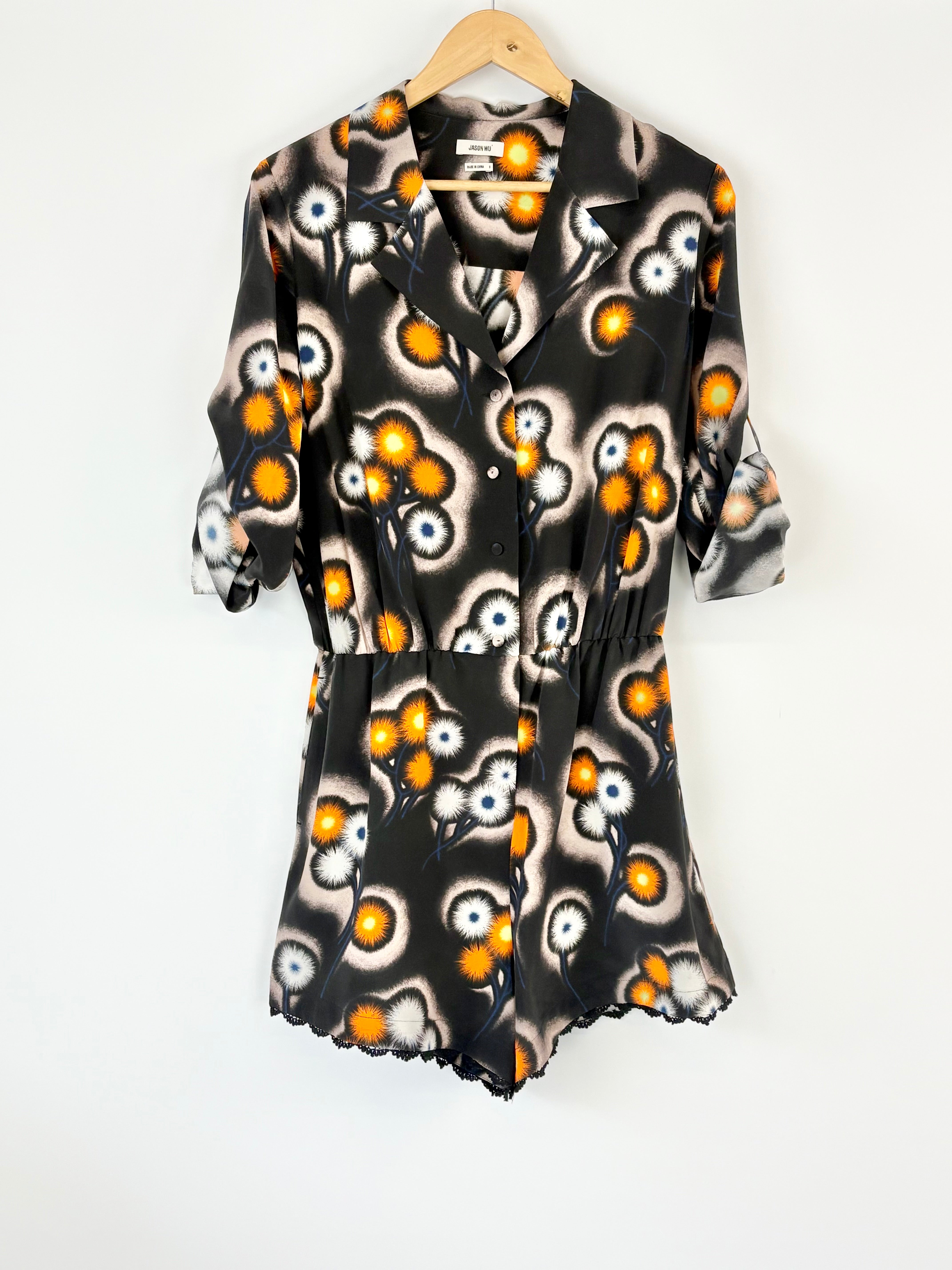 Black playsuit with orange and white abstract pattern on a hanger against a white background
