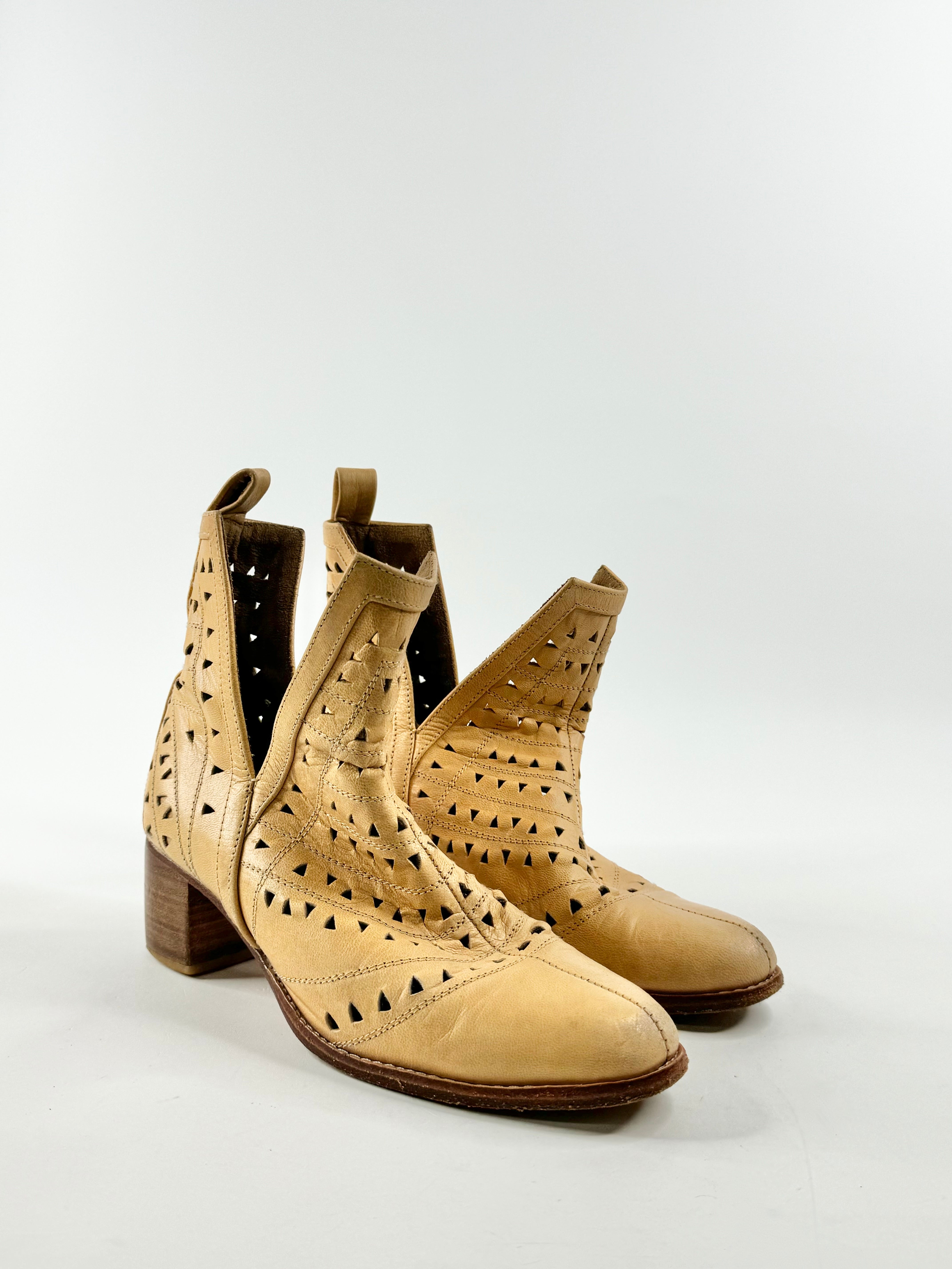 A pair of mustard yellow ankle boots with laser cut patterns, a small heel, and rounded toes.