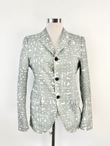 A Jil Sander grey text pattern blazer on a mannequin, featuring a tailored fit, collar, and three-button front.