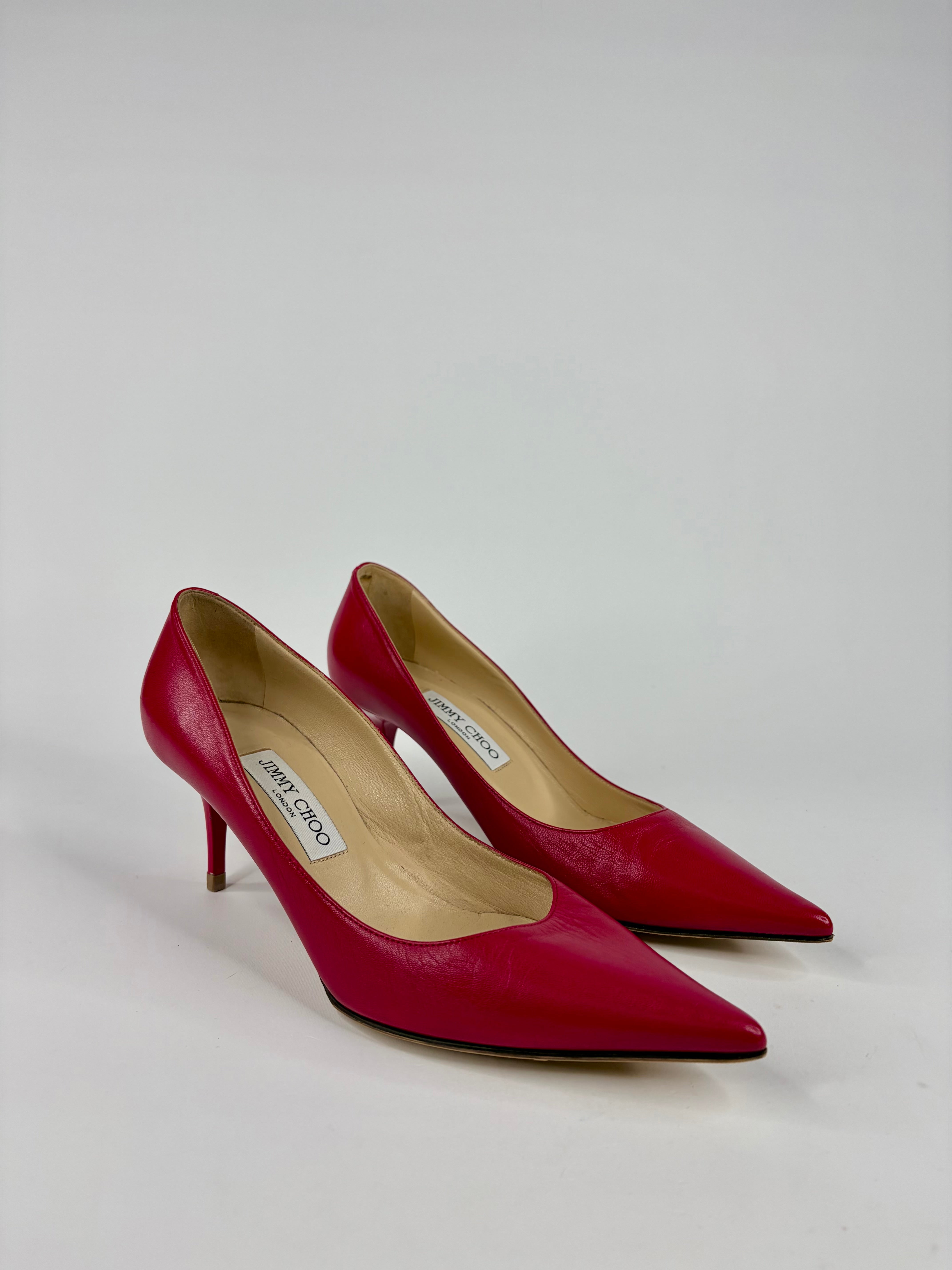 Red high-heeled shoes with 'Jimmy Choo' label on a light gray background