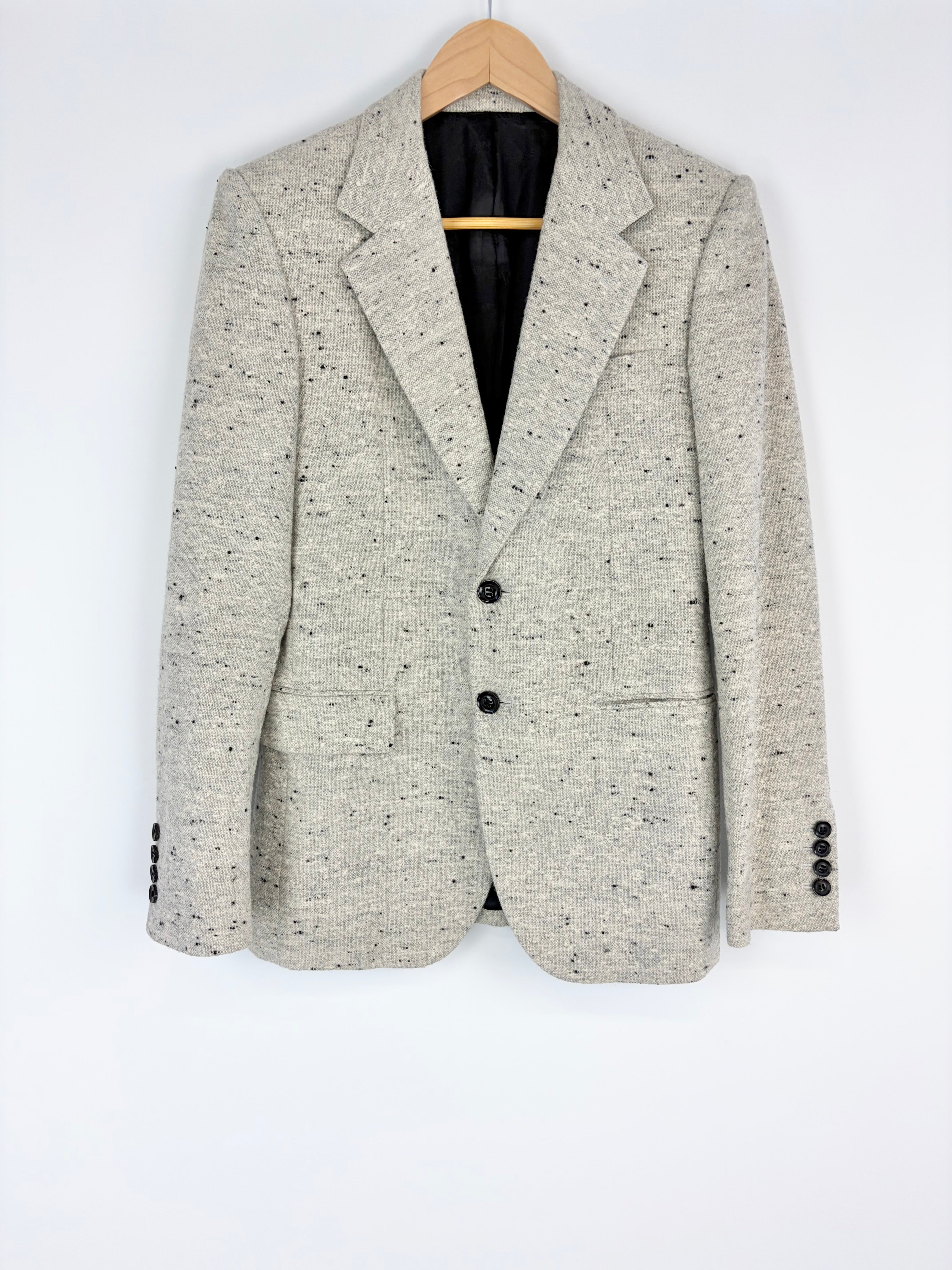 Light gray blazer with black speckles on a hanger against a white background