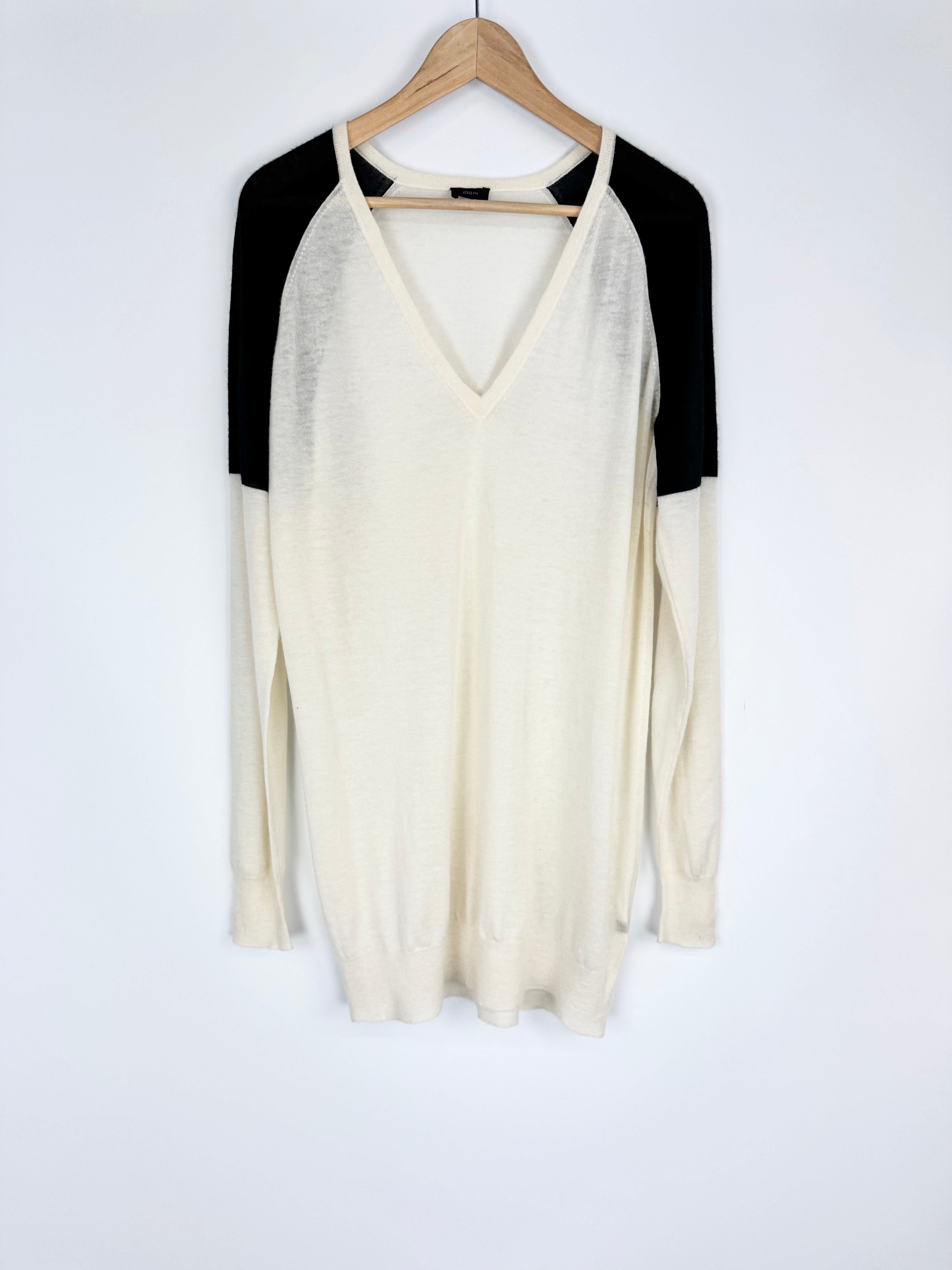 White long-sleeve top with black sleeves on a wooden hanger against a white background