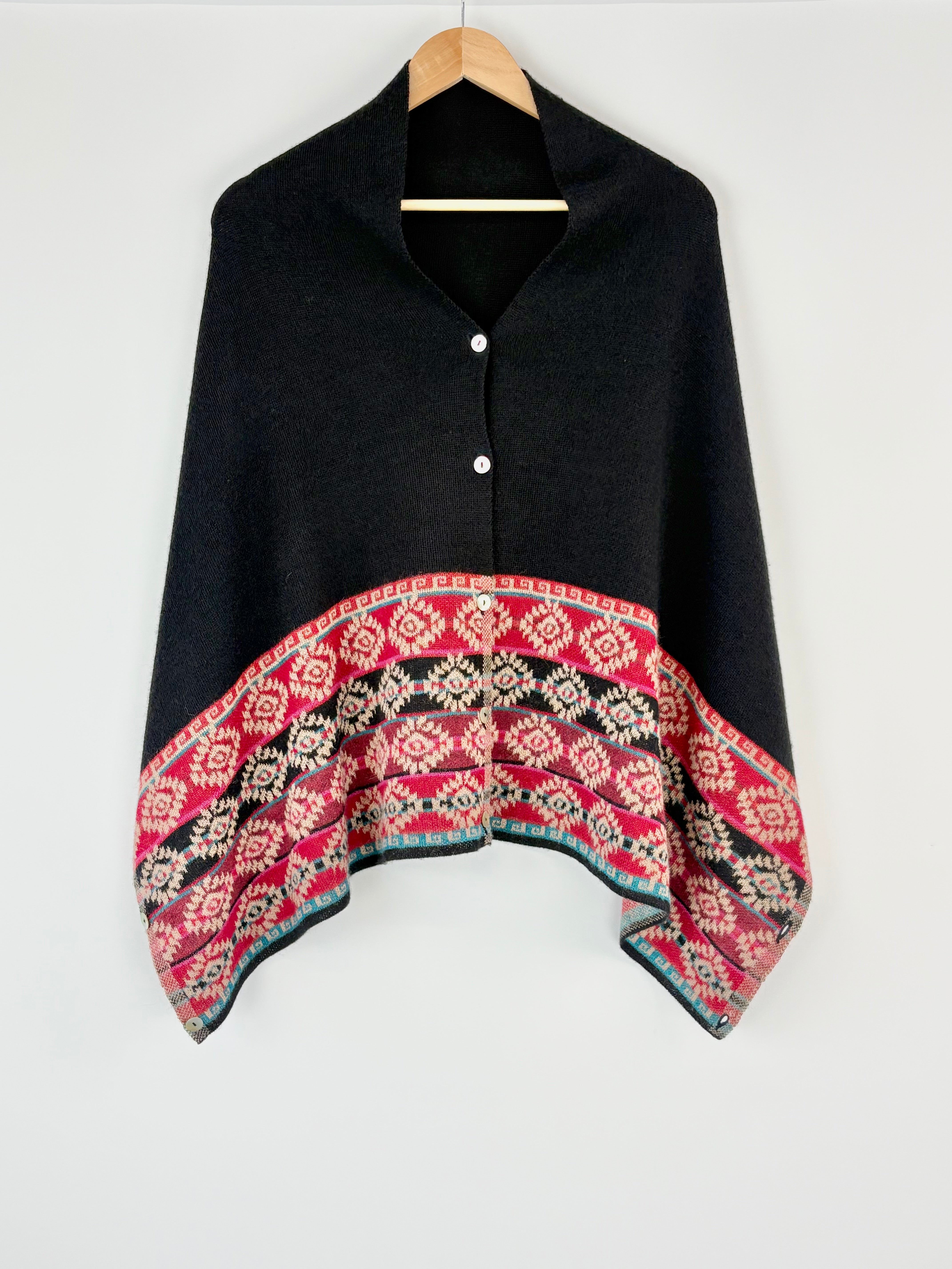 Black poncho with a colorful patterned hem on a white background