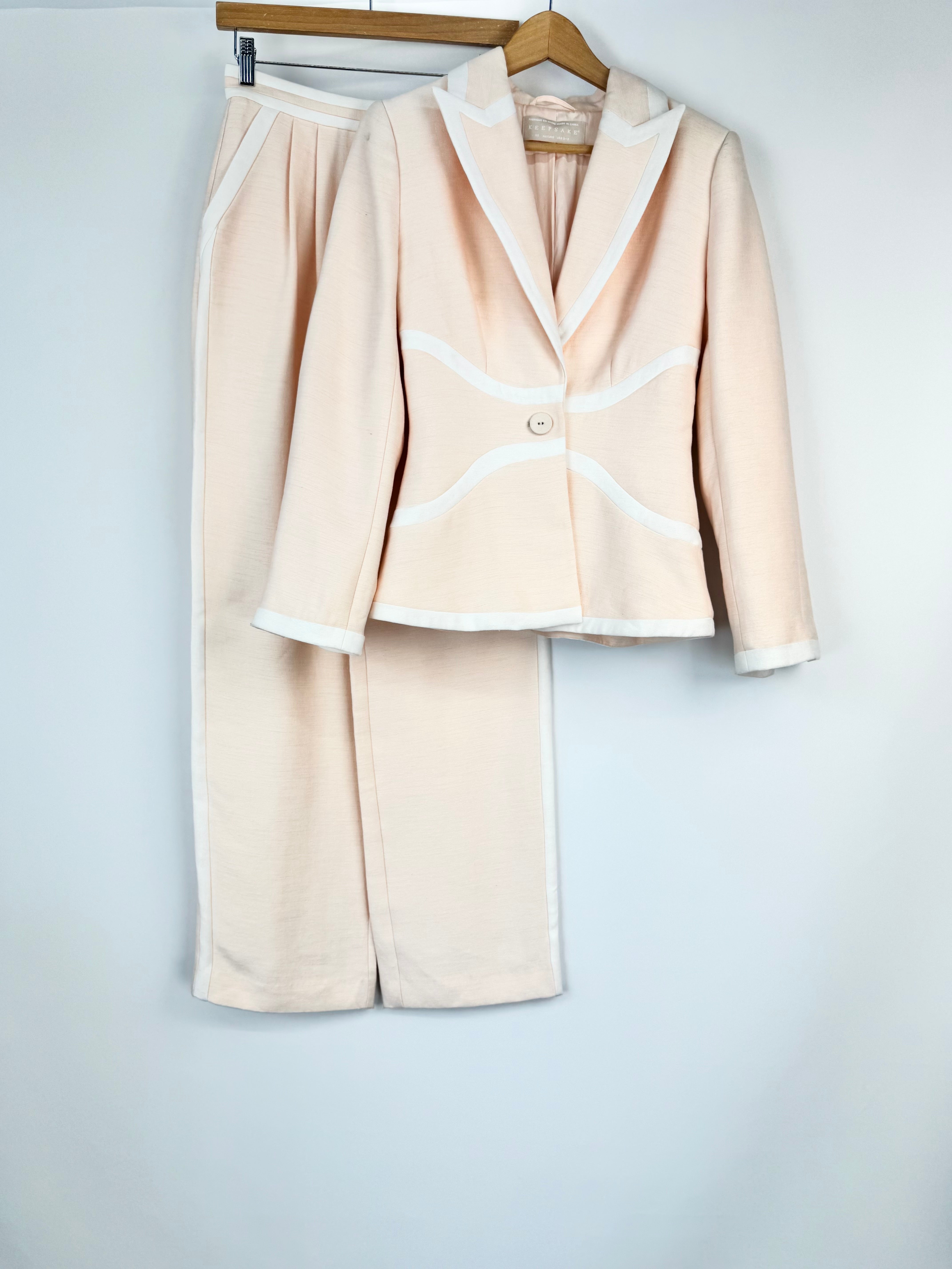 Beige suit with white trim on a hanger against a light gray background