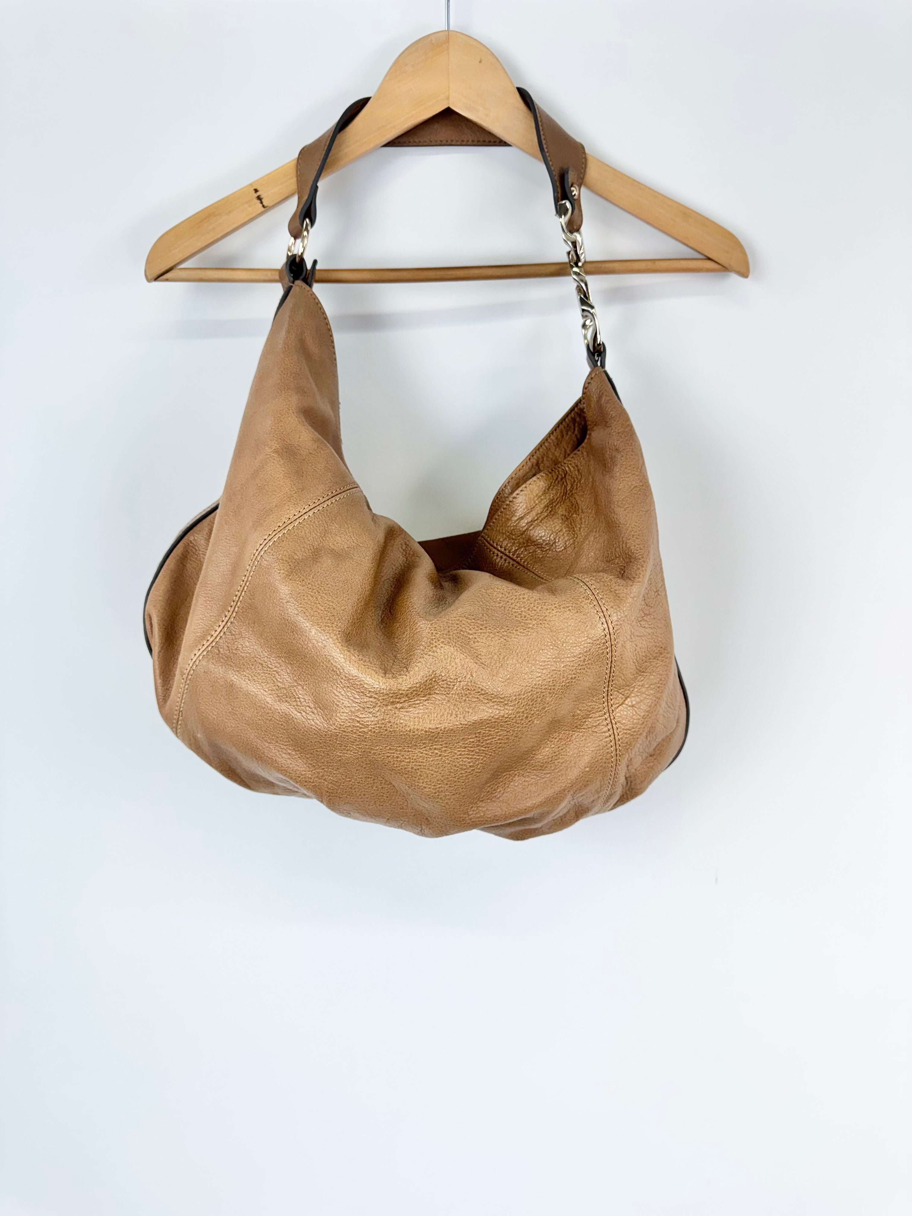 Brown leather handbag on a wooden hanger against a white background