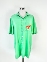 A green short-sleeved shirt displayed on a mannequin, featuring a small red and yellow lobster graphic on the front.