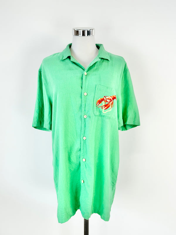 A green short-sleeved shirt displayed on a mannequin, featuring a small red and yellow lobster graphic on the front.