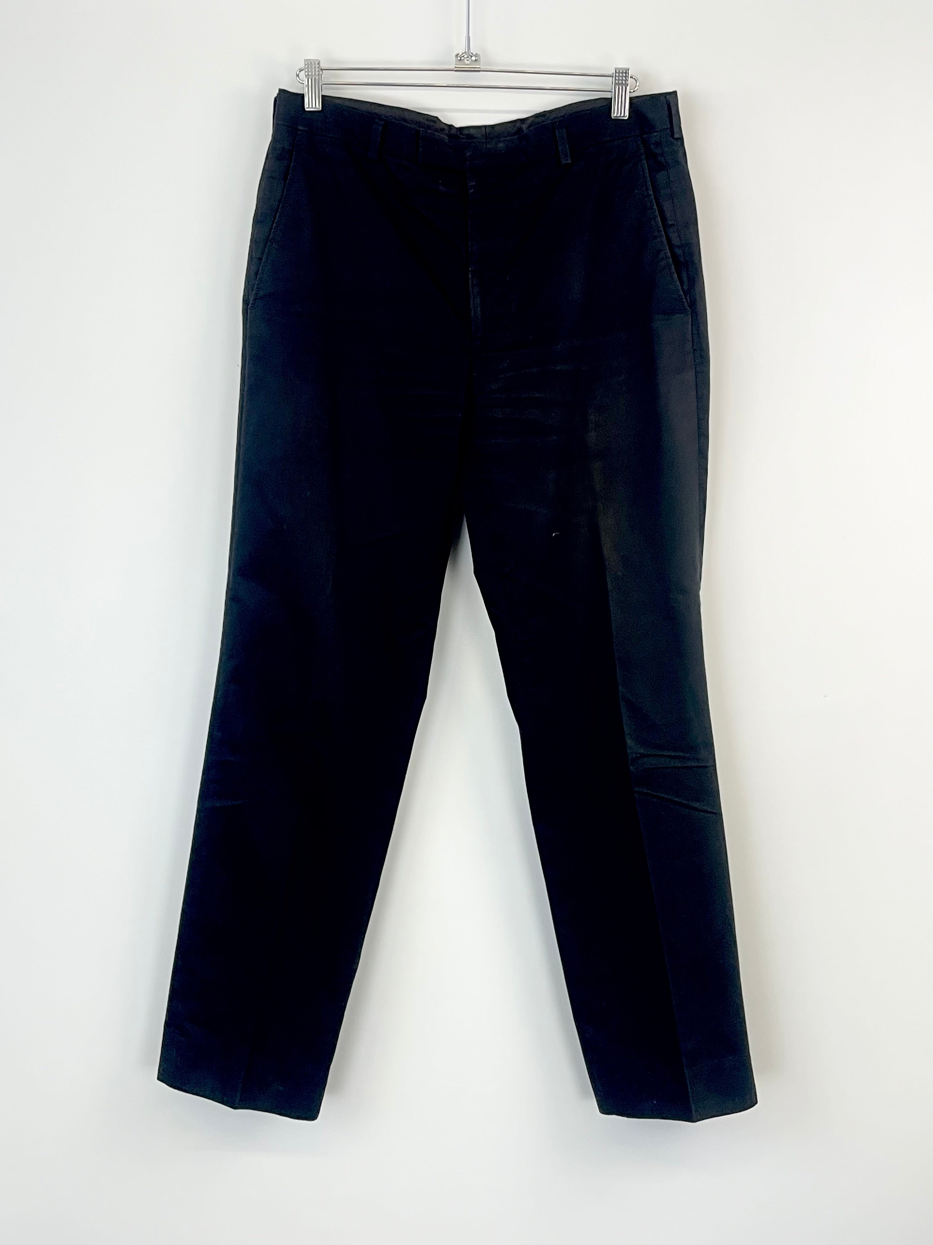 A pair of black cotton trousers hanging against a white background.