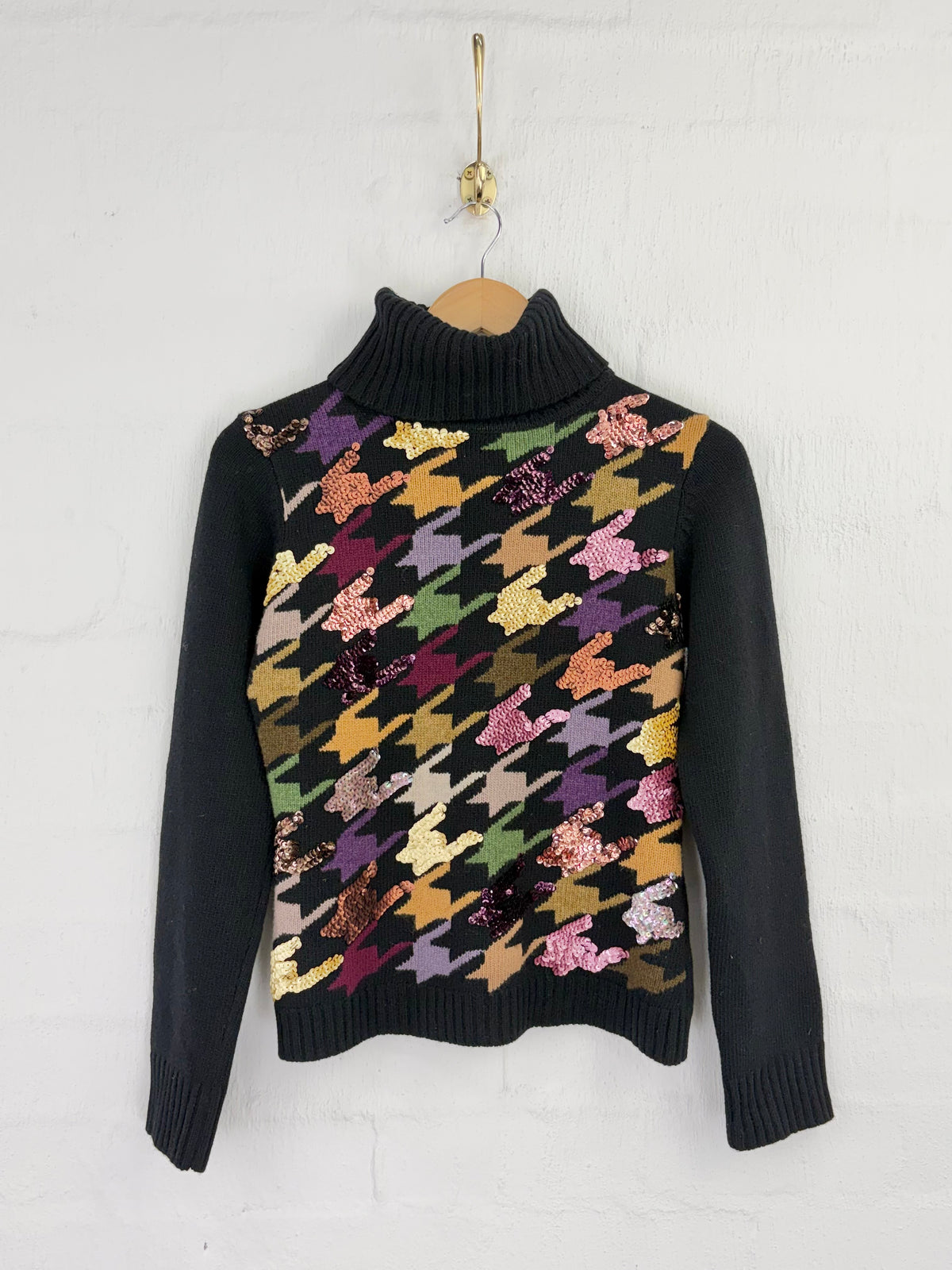 A black turtleneck jumper with multcolour houndstooth patterns on the body & sequin embellishment against a white background. 