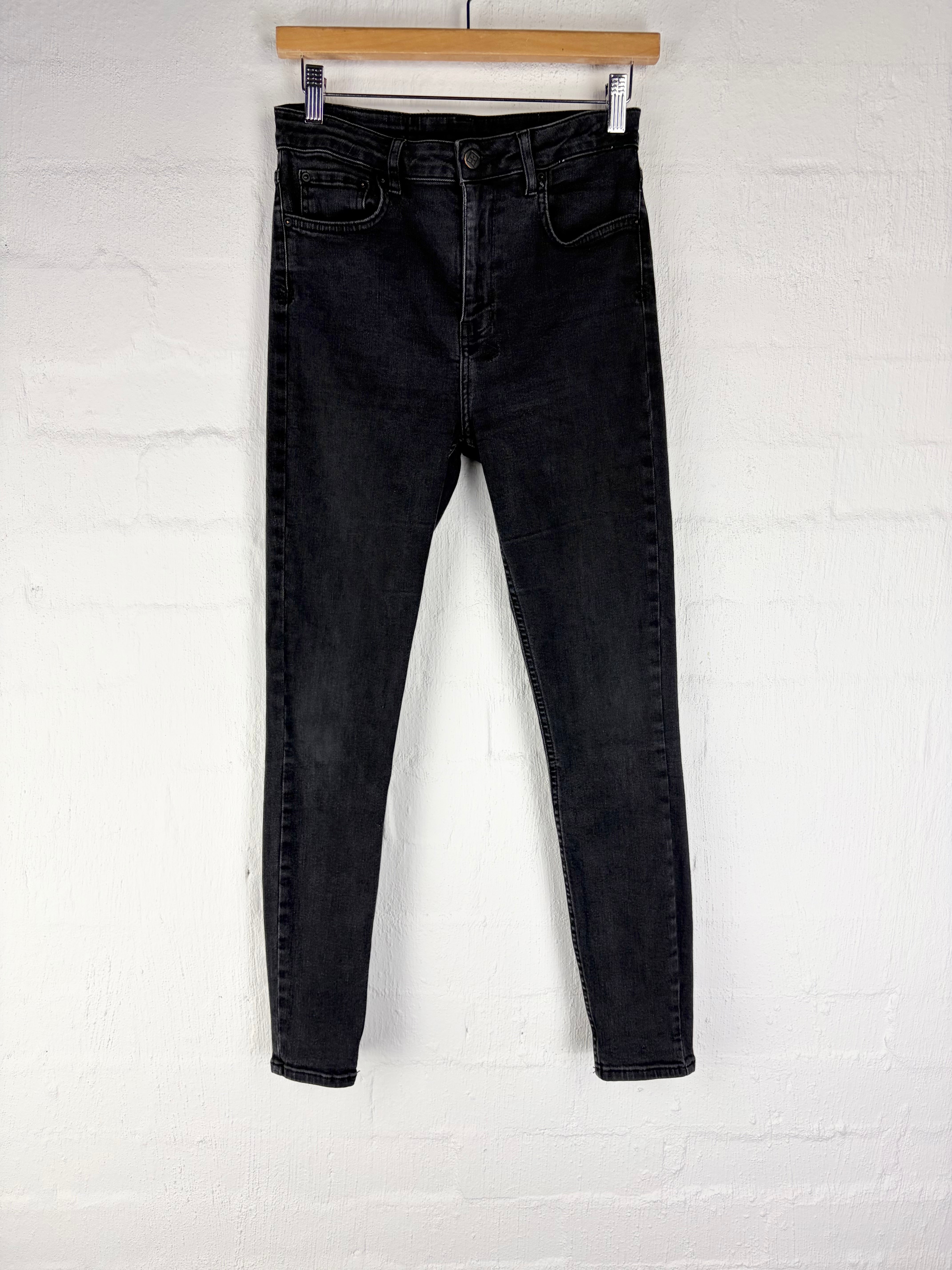 Black skinny jeans hanging from a wooden hanger against a white painted brick wall.