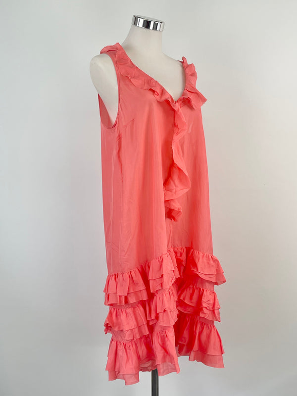 A flamingo colored, silk ruffle-tiered dress on a mannequin. The dress features a sleeveless design with a v-neck and tiered ruffle detailing throughout.