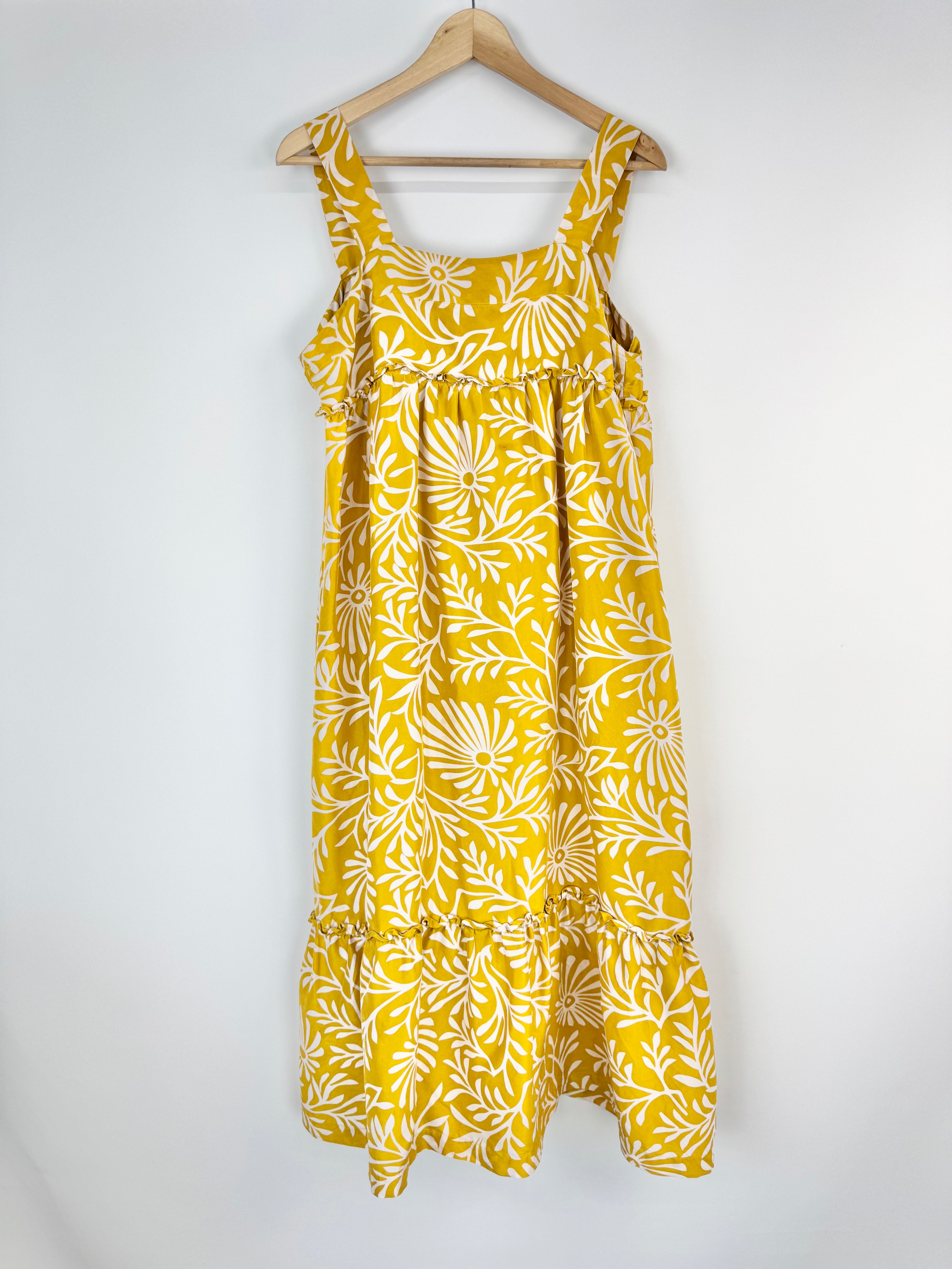 Yellow dress with white floral pattern on a hanger against a white background
