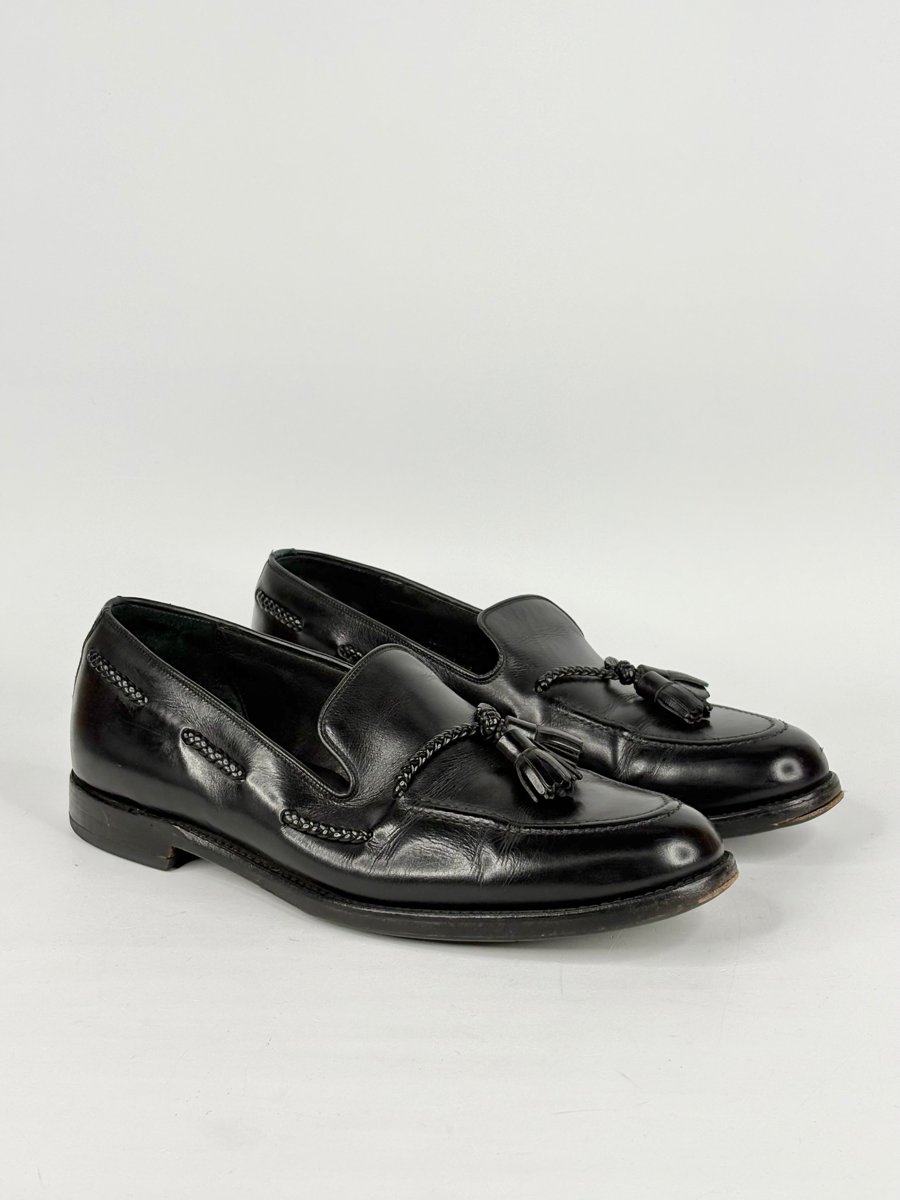 Pair of black loafers with tassels on a light gray background