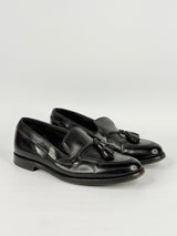 Pair of black loafers with tassels on a light gray background