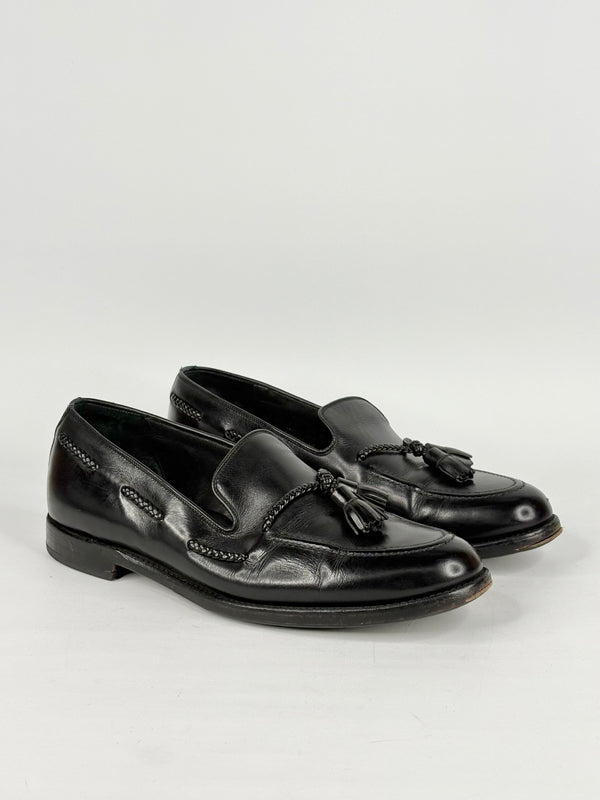 Pair of black loafers with tassels on a light gray background