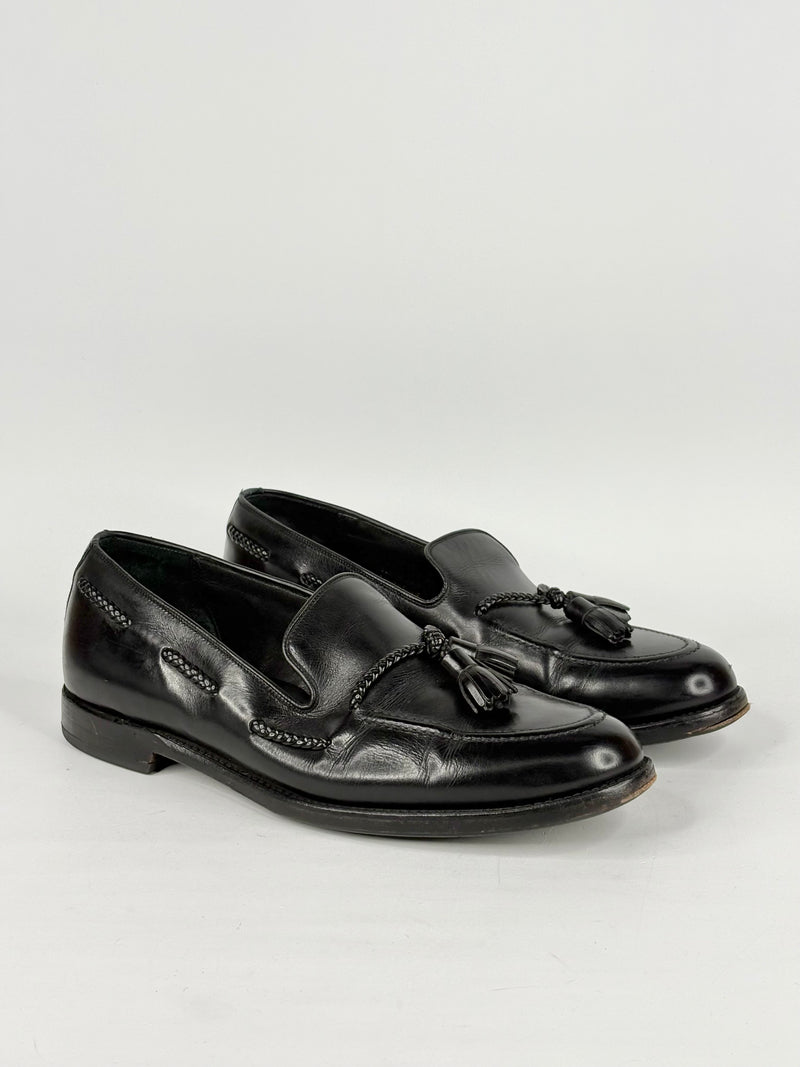 Pair of black loafers with tassels on a light gray background