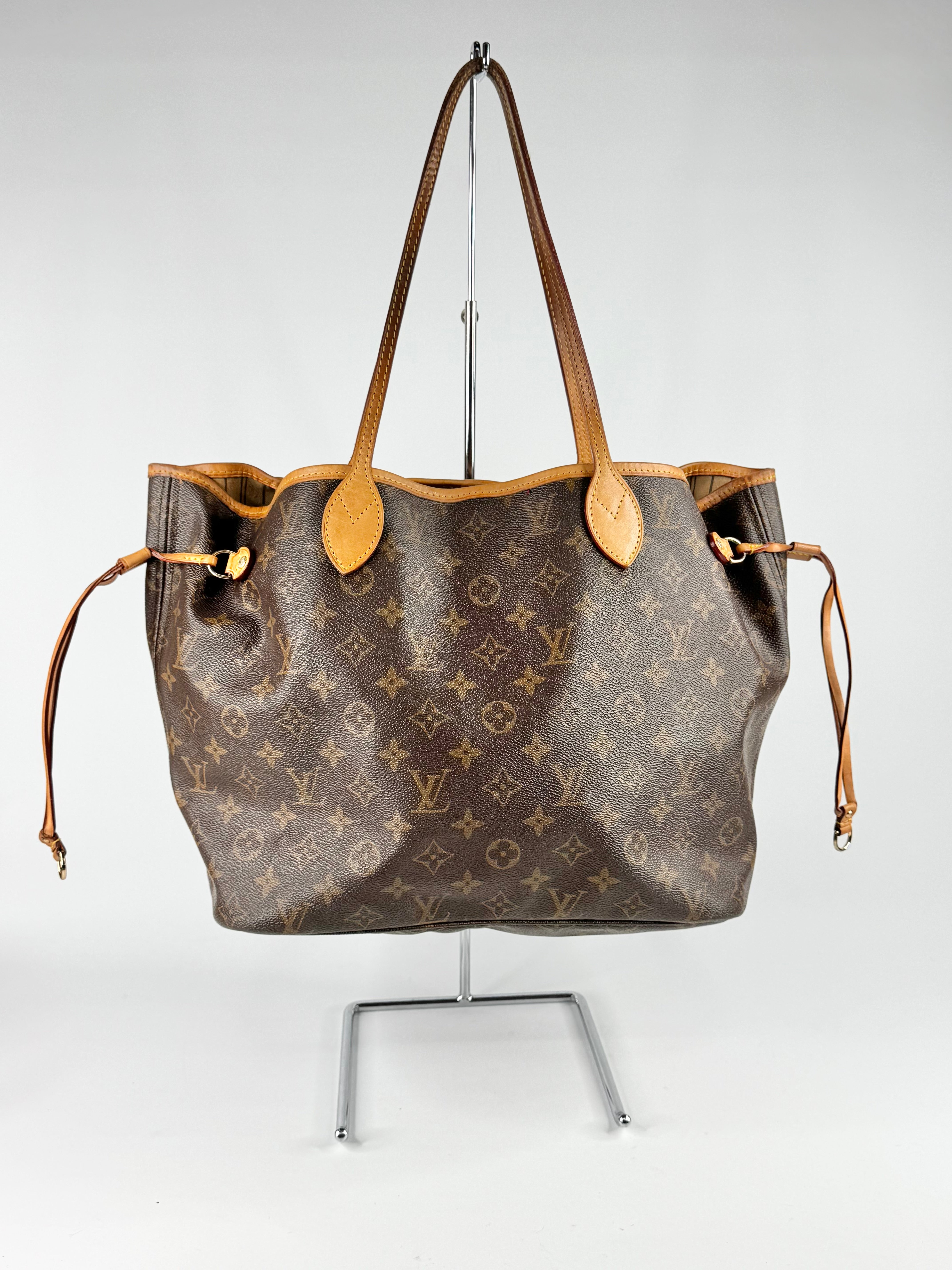 Louis Vuitton handbag with monogram pattern on a stand against a white background