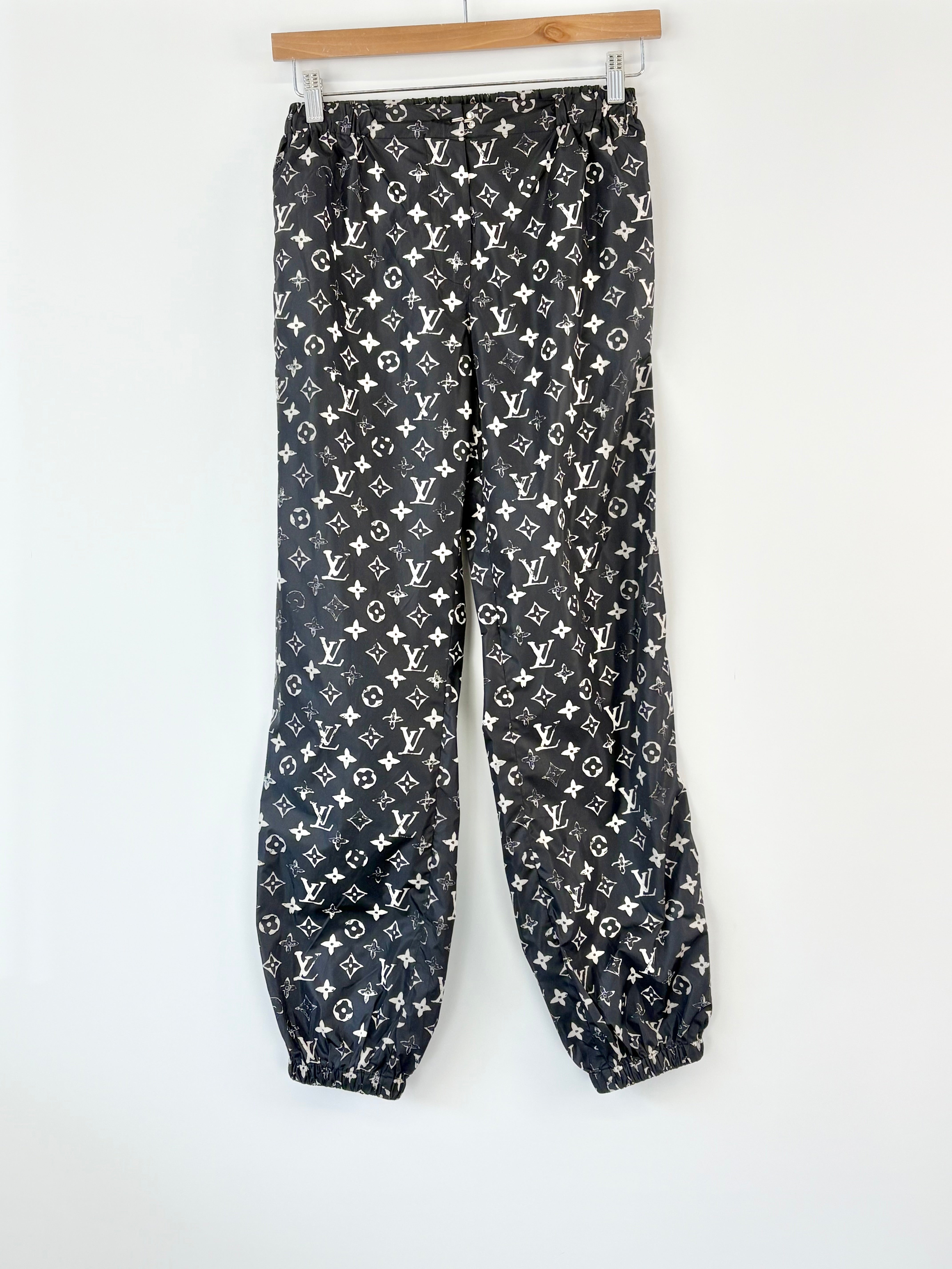 Black pants with white monogram pattern hanging on a wooden hanger against a white background